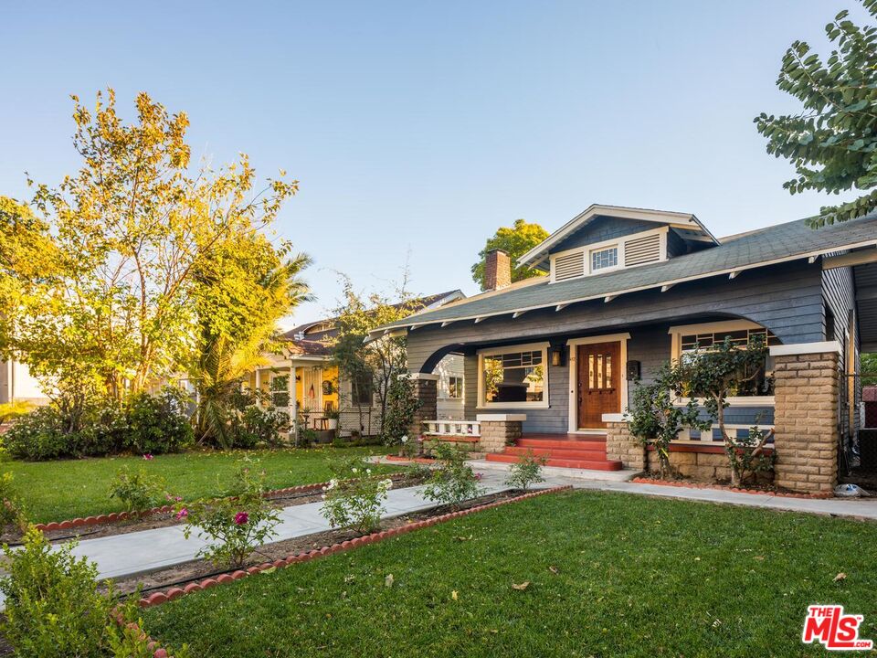 Blue Craftsman-style home with a covered porch, brick columns, red door, and landscaped front lawn.