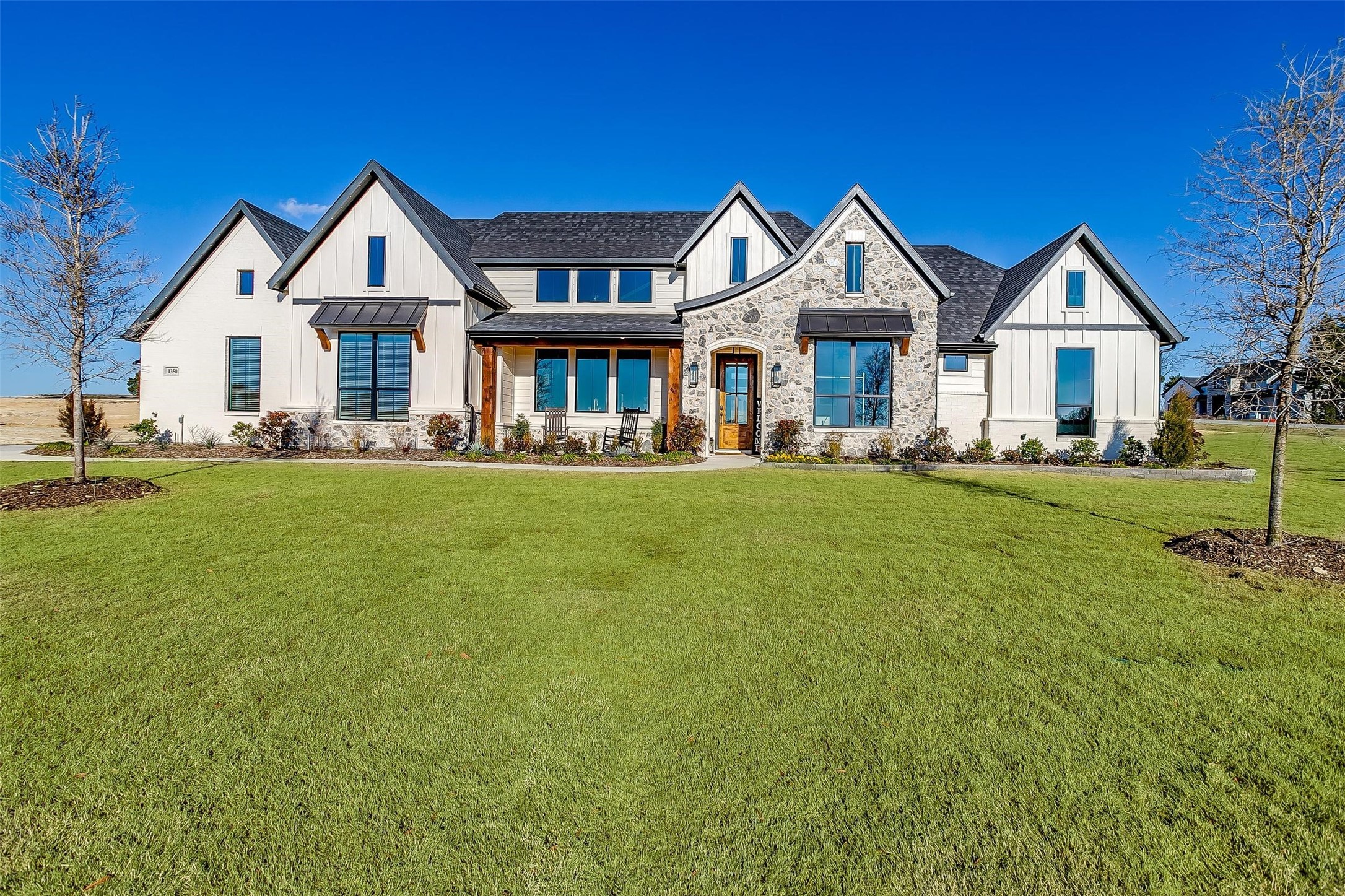 Large white-and-stone home with multiple gables and a broad green lawn.