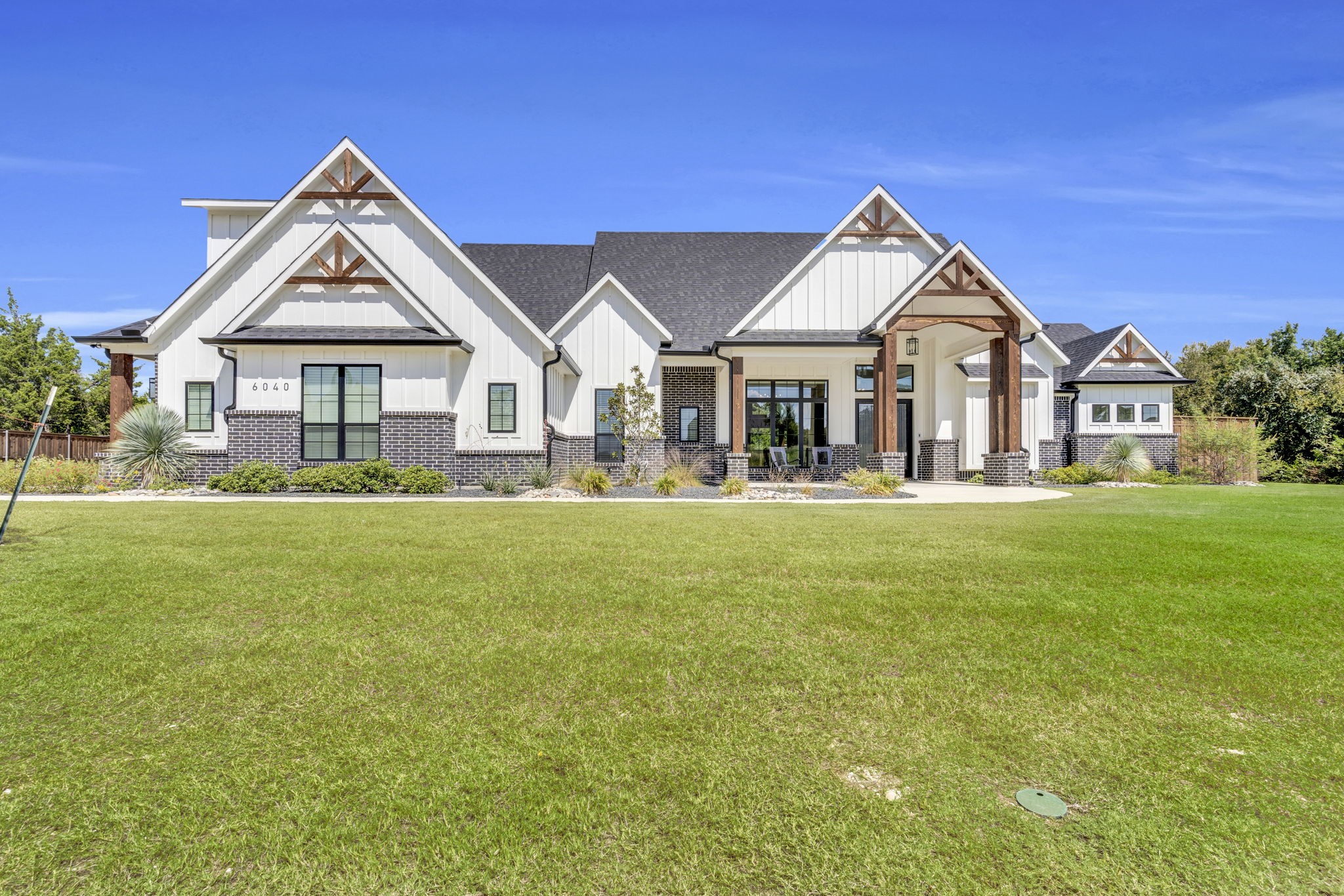 White-sided building with brick accents and timber-trimmed gables behind a broad lawn.