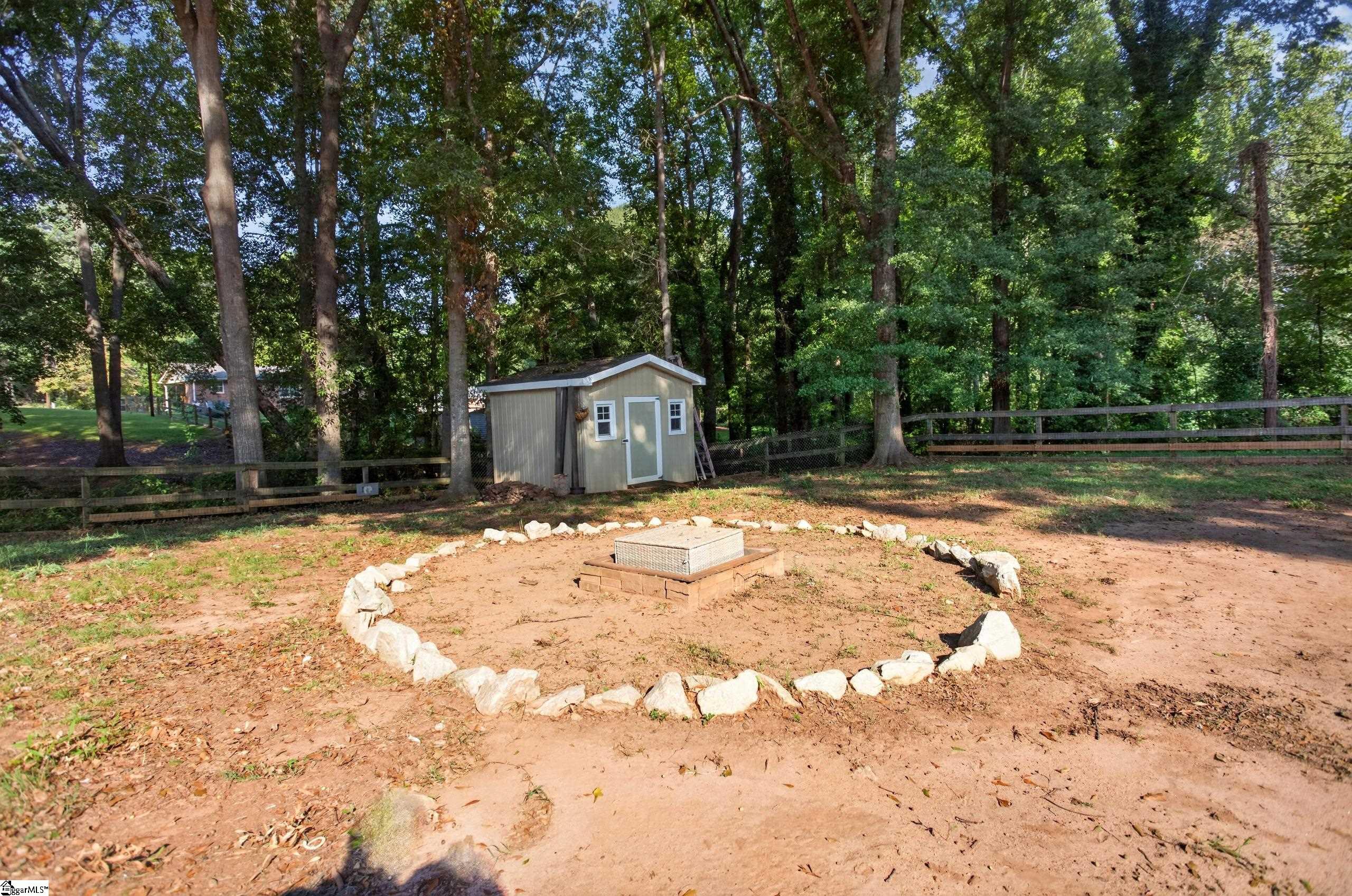 Wooded backyard with a gray shed, fenced perimeter, and a stone-edged circular area.