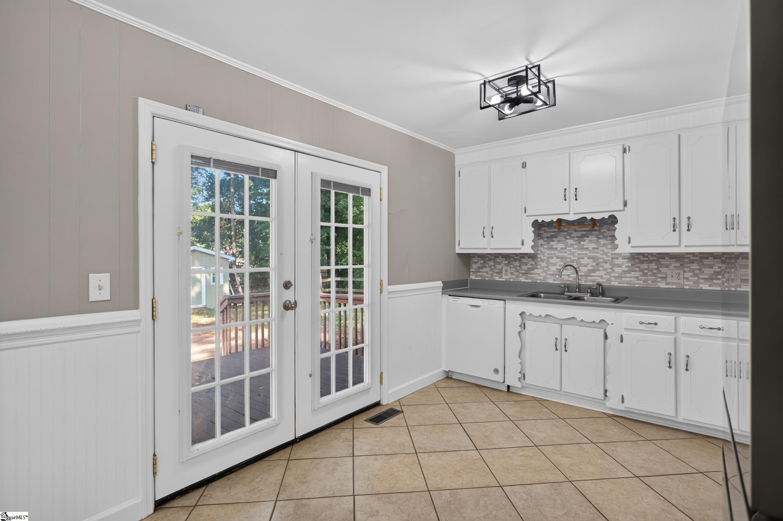 Kitchen with white cabinets and tiled backsplash beside glass doors opening to a deck.