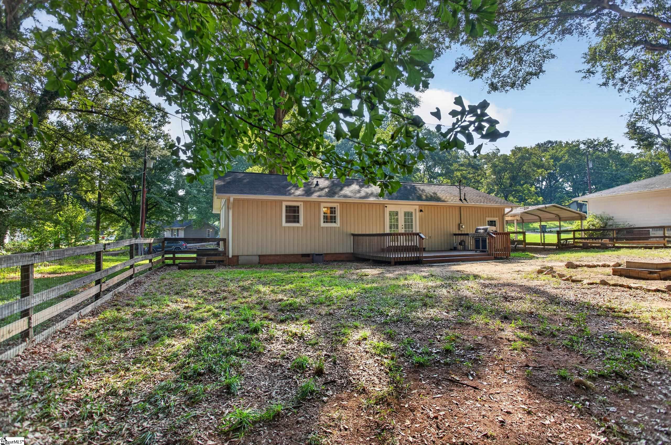 Tan single-story home with a raised deck and grill in a leafy fenced backyard.