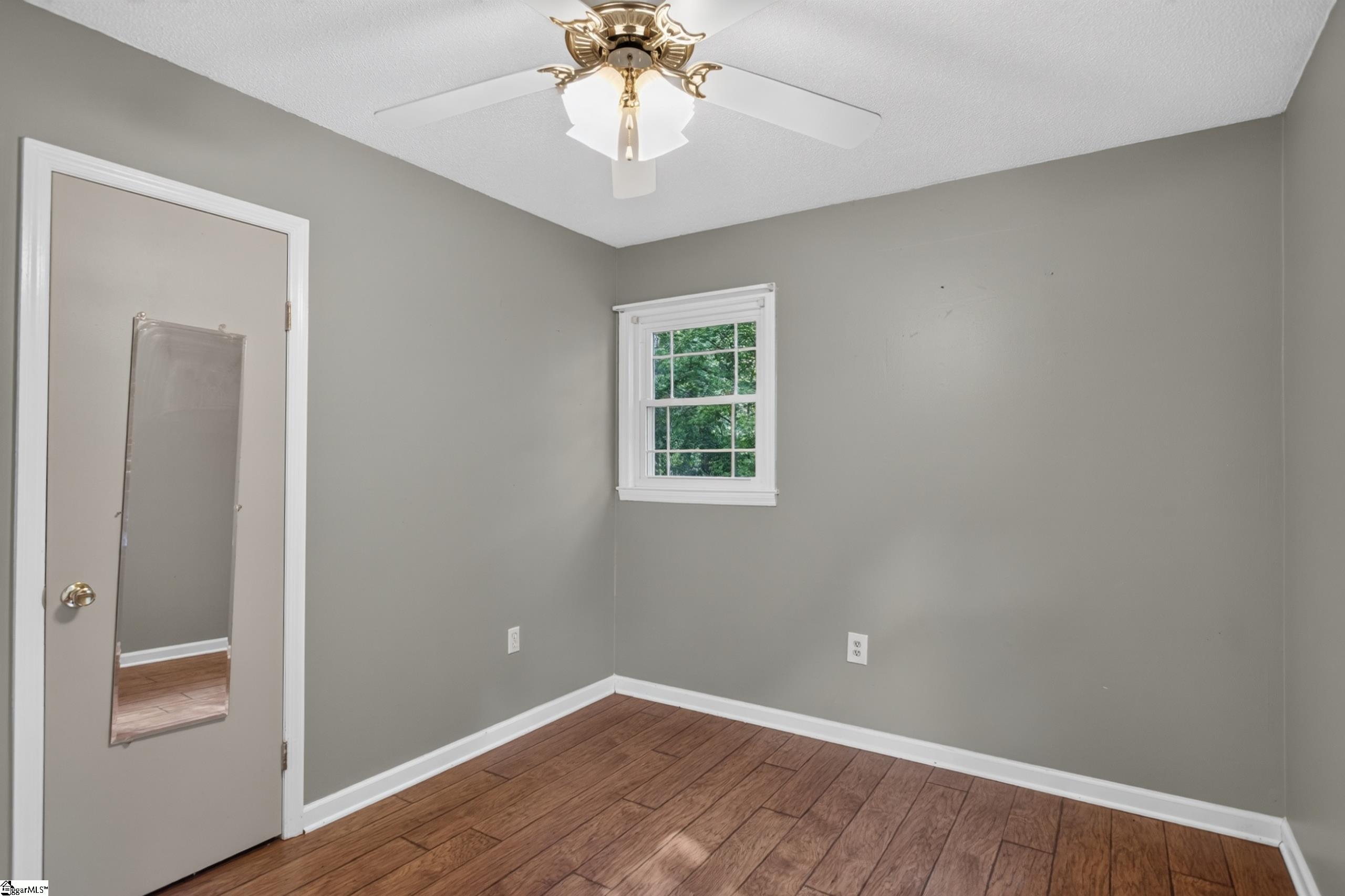 Empty bedroom with gray walls, wood-look flooring, a mirrored door, and a ceiling fan.