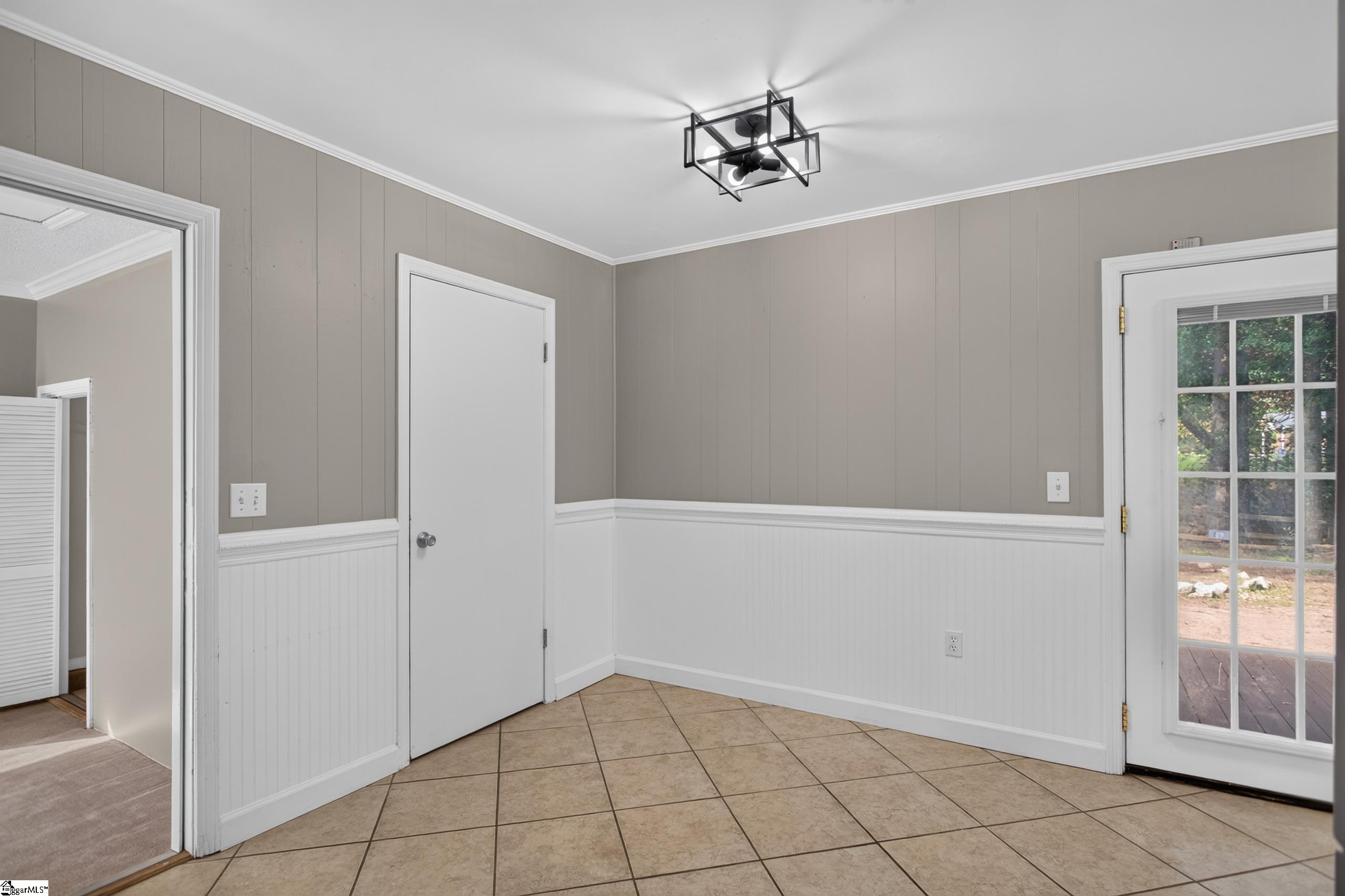 Empty tiled room with white wainscoting and a glass-paneled door to the deck.