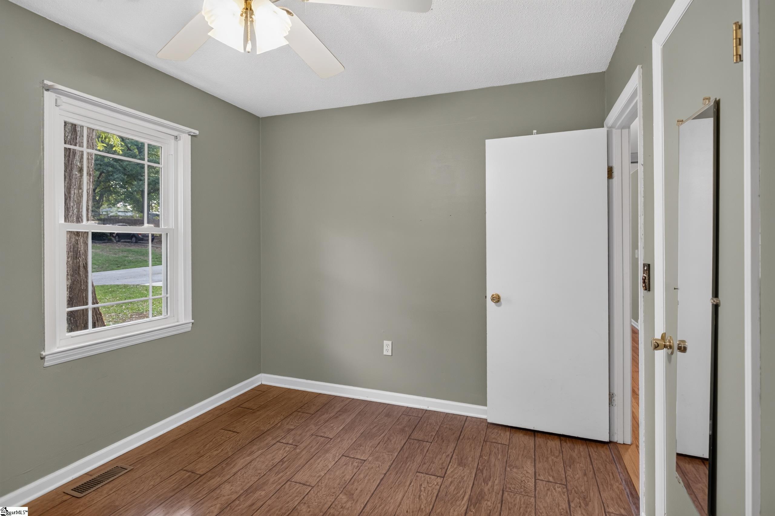 Empty room with wood-look flooring, a white-trimmed window, and a ceiling fan.