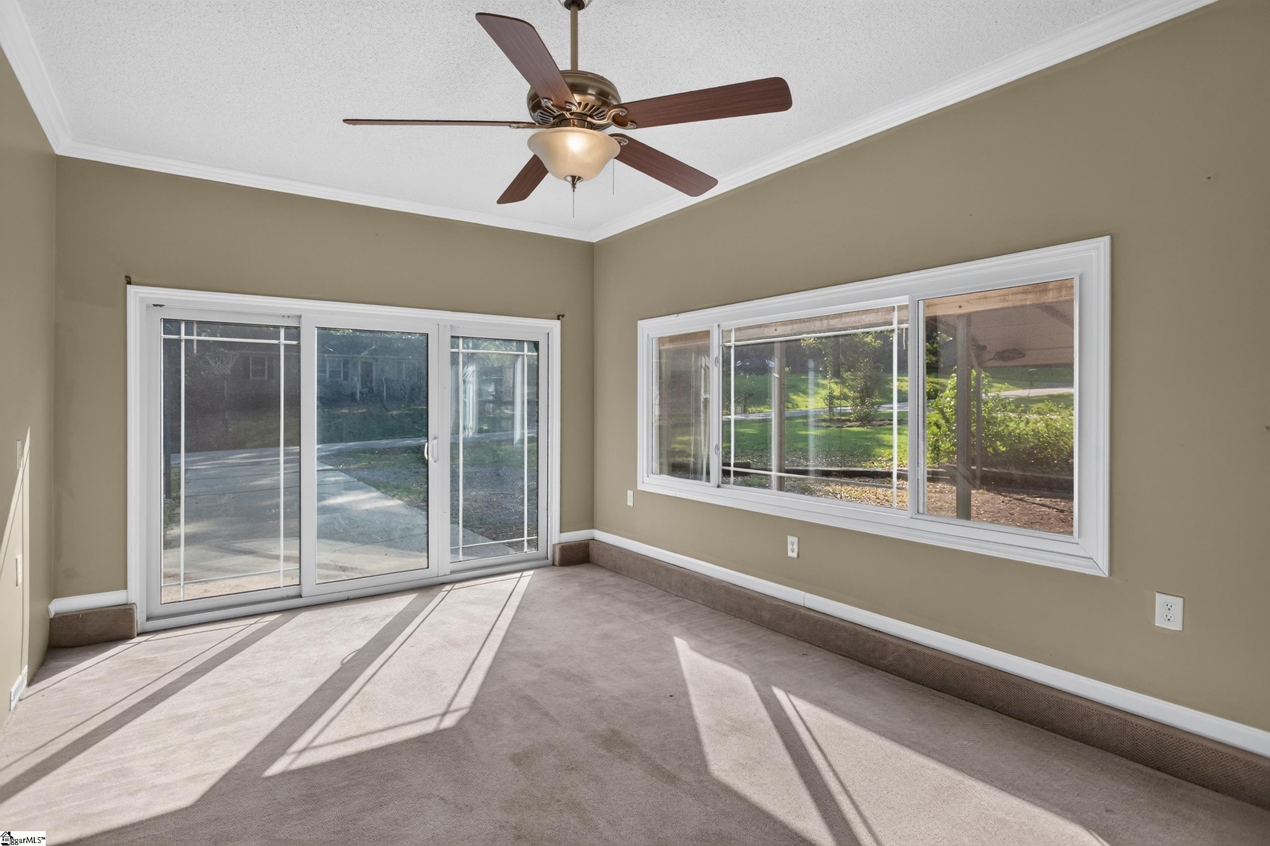 Carpeted room with a ceiling fan, sliding glass doors, and wide windows facing the yard.