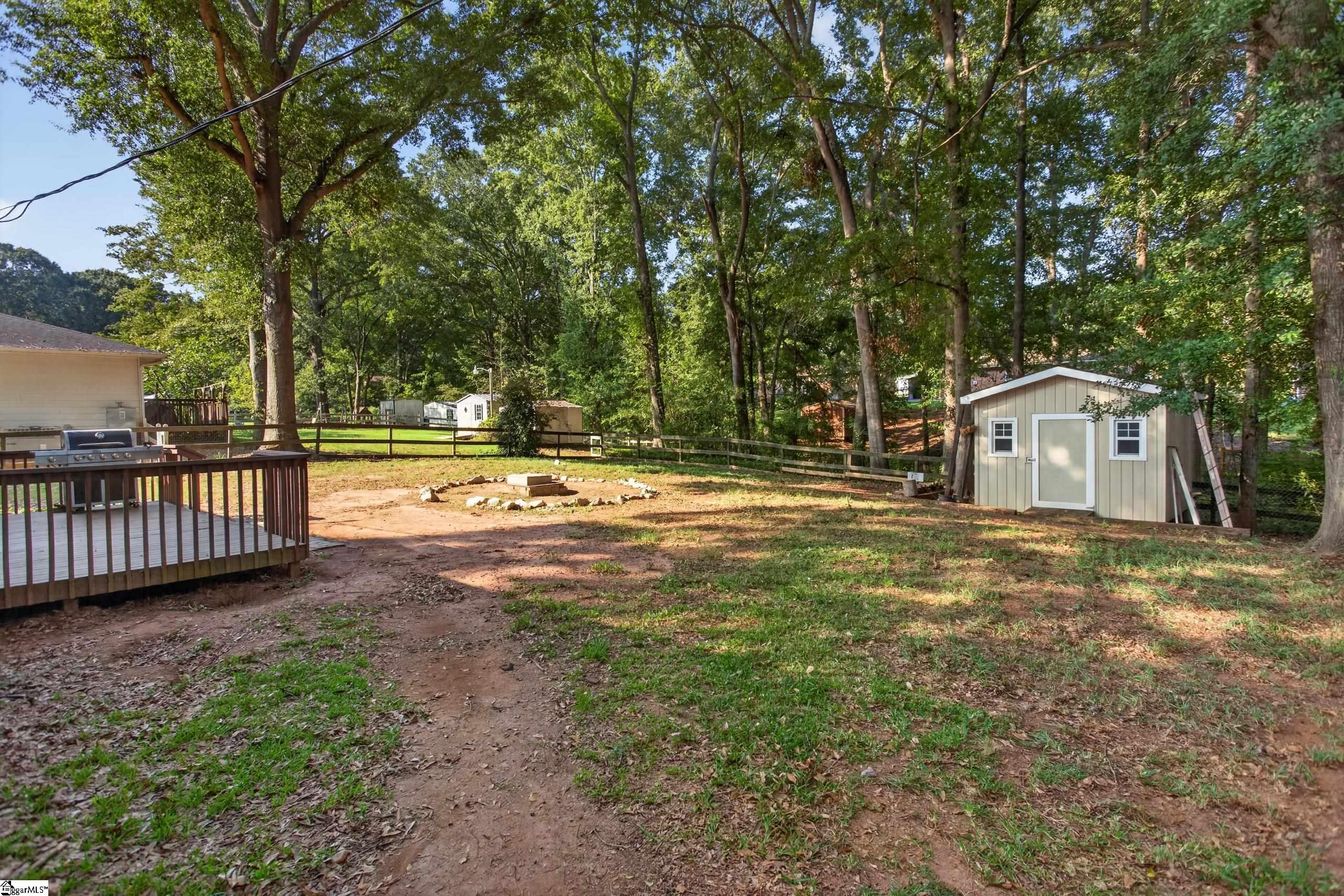 Wooded backyard with a deck, fire pit, fenced yard, and beige storage shed.