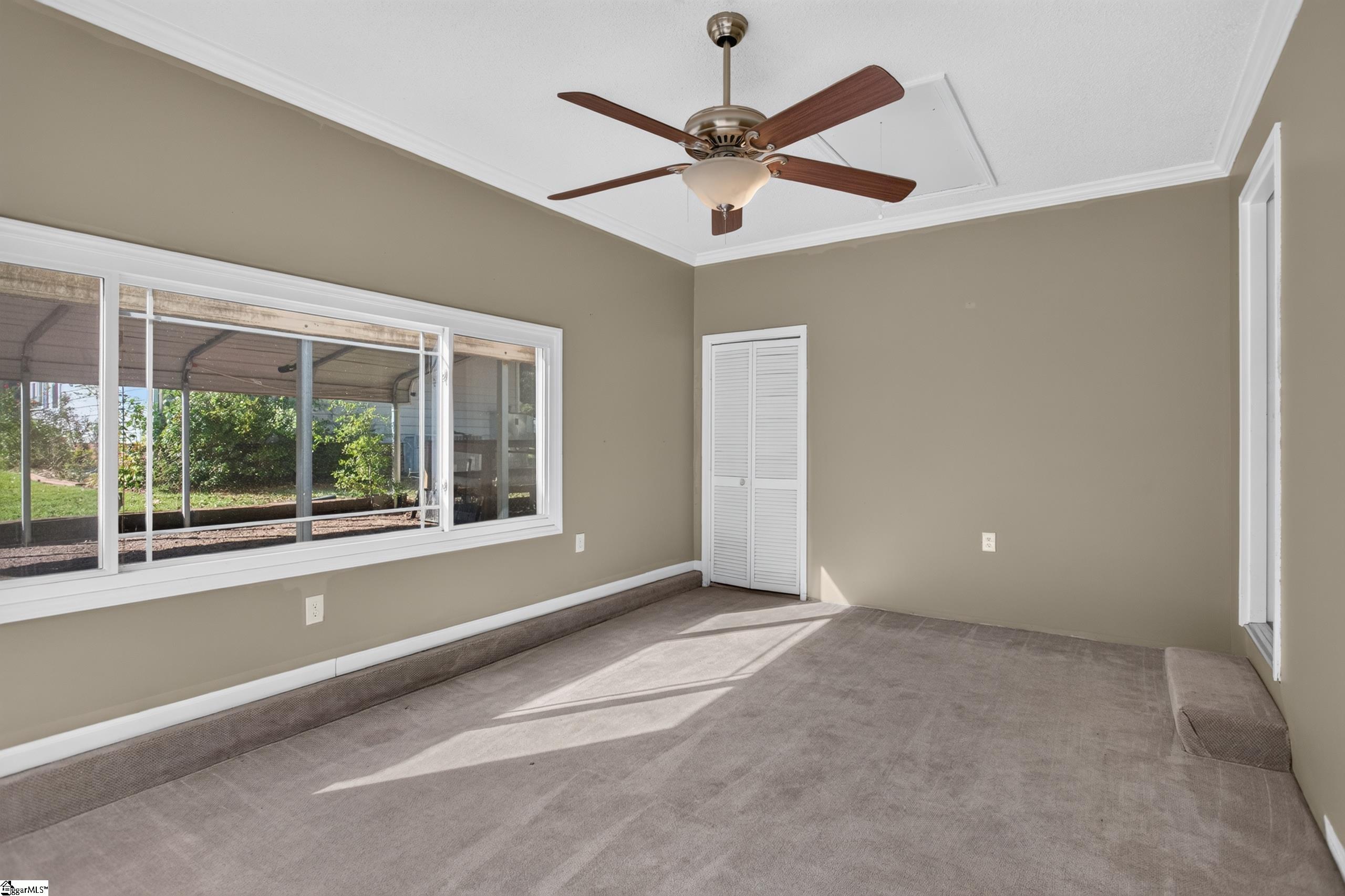 Empty carpeted room with a ceiling fan and wide windows overlooking a covered patio.