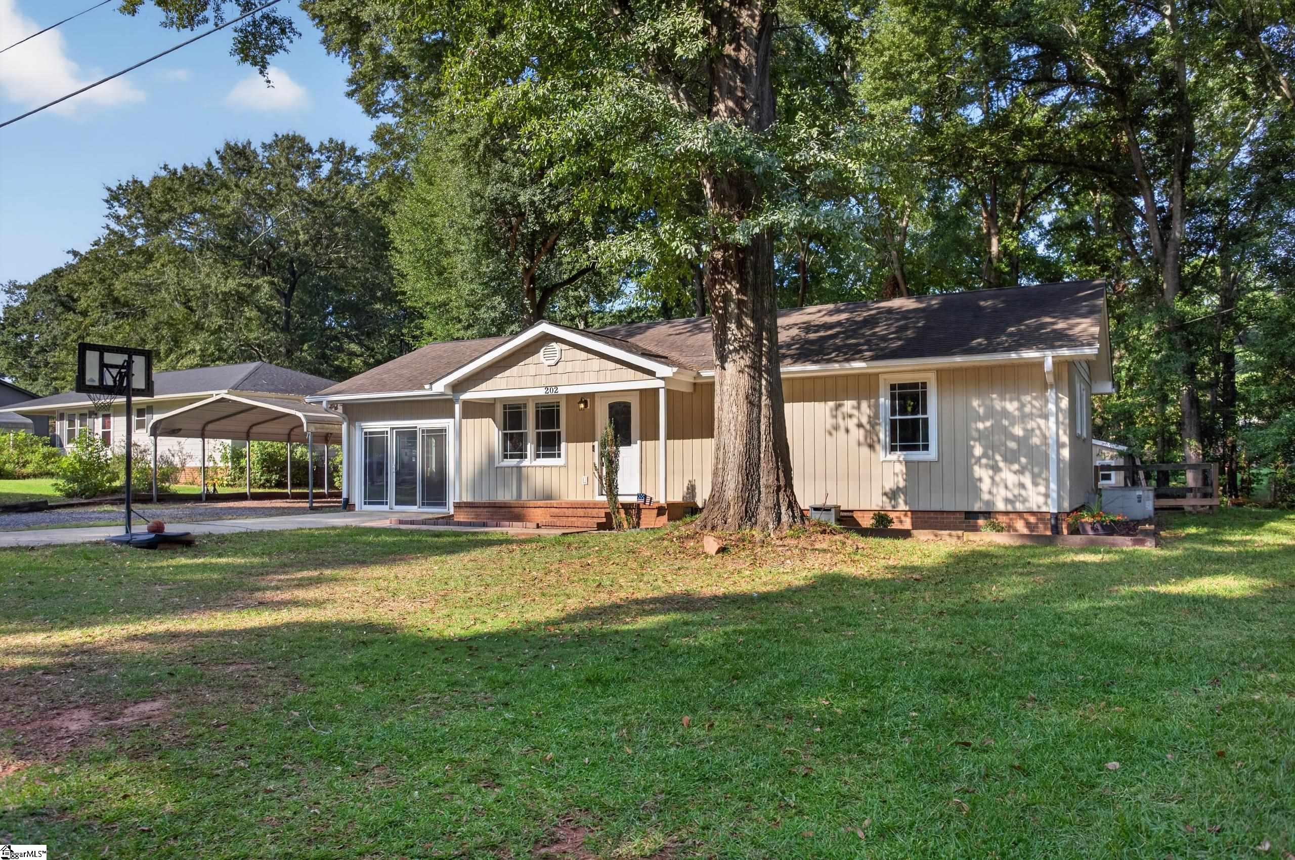 Beige one-story home with a large front-yard tree, covered carport, and basketball hoop.