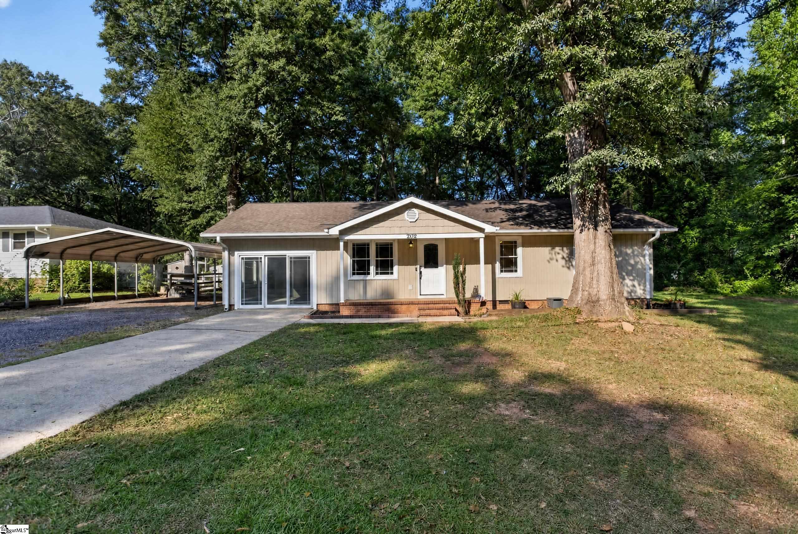 Single-story tan home with a covered entry, carport, driveway, and large shade trees.