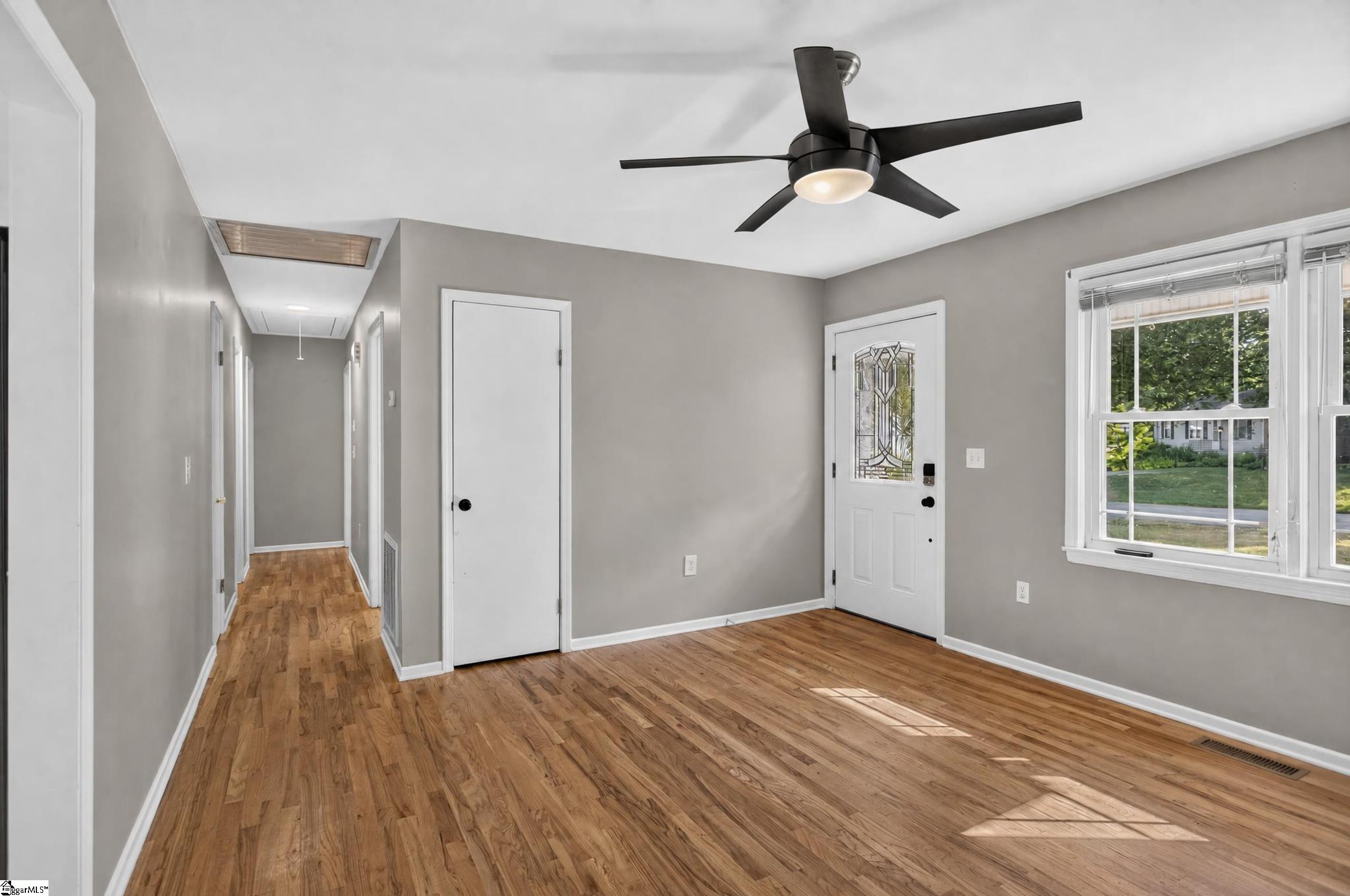Vacant living room with hardwood floors, a black ceiling fan, and a decorative glass front door.
