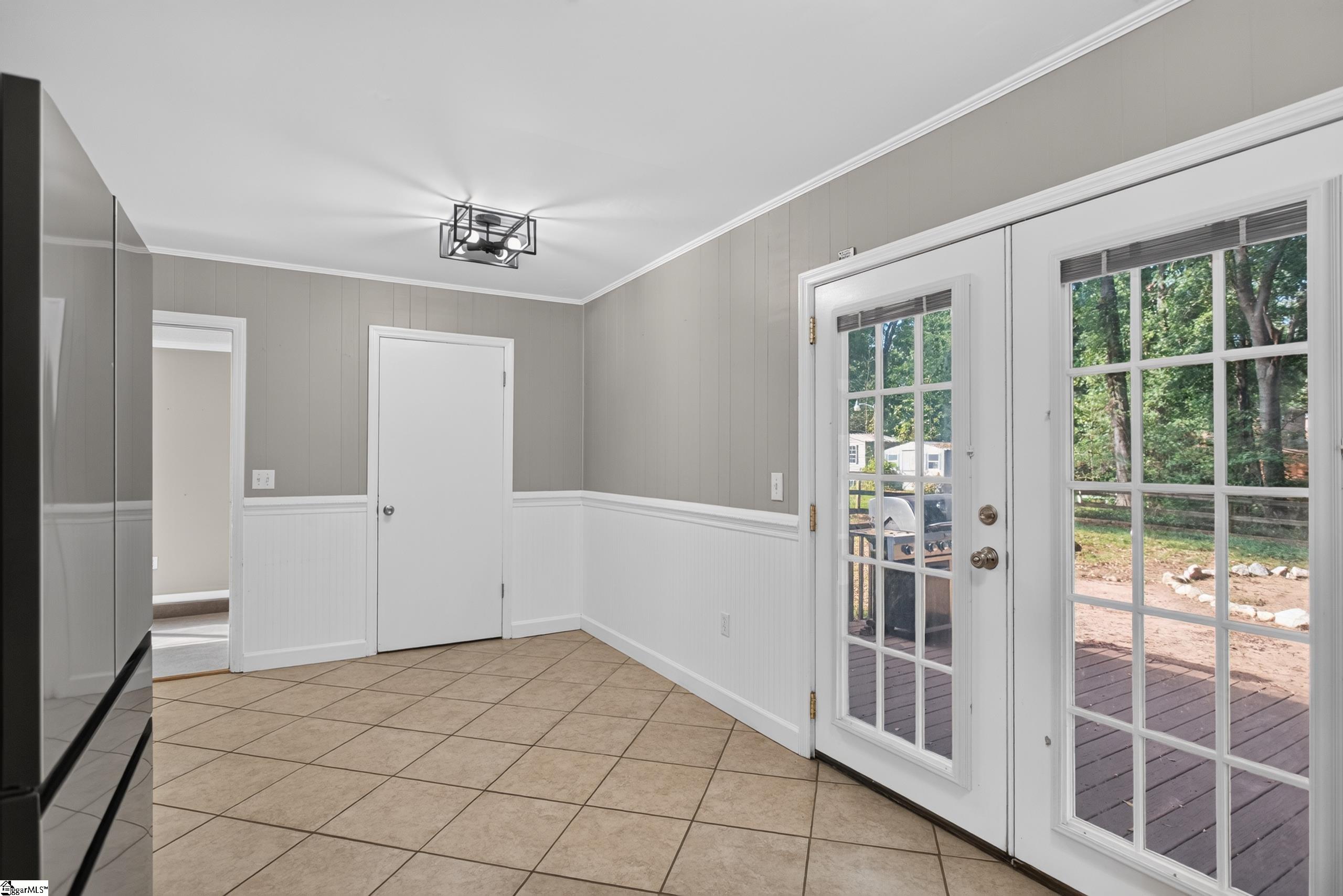Unfurnished tiled kitchen area with French doors opening onto a wooden deck and leafy yard.