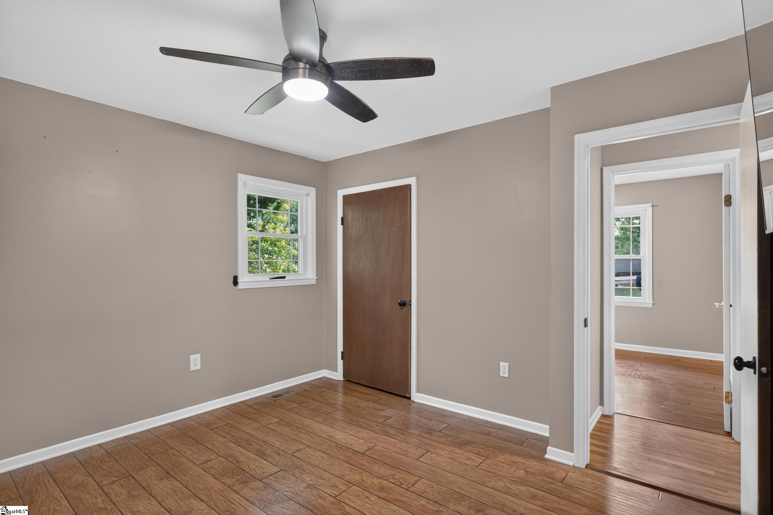 Empty room with wood-look flooring, a ceiling fan, and a doorway to another room.