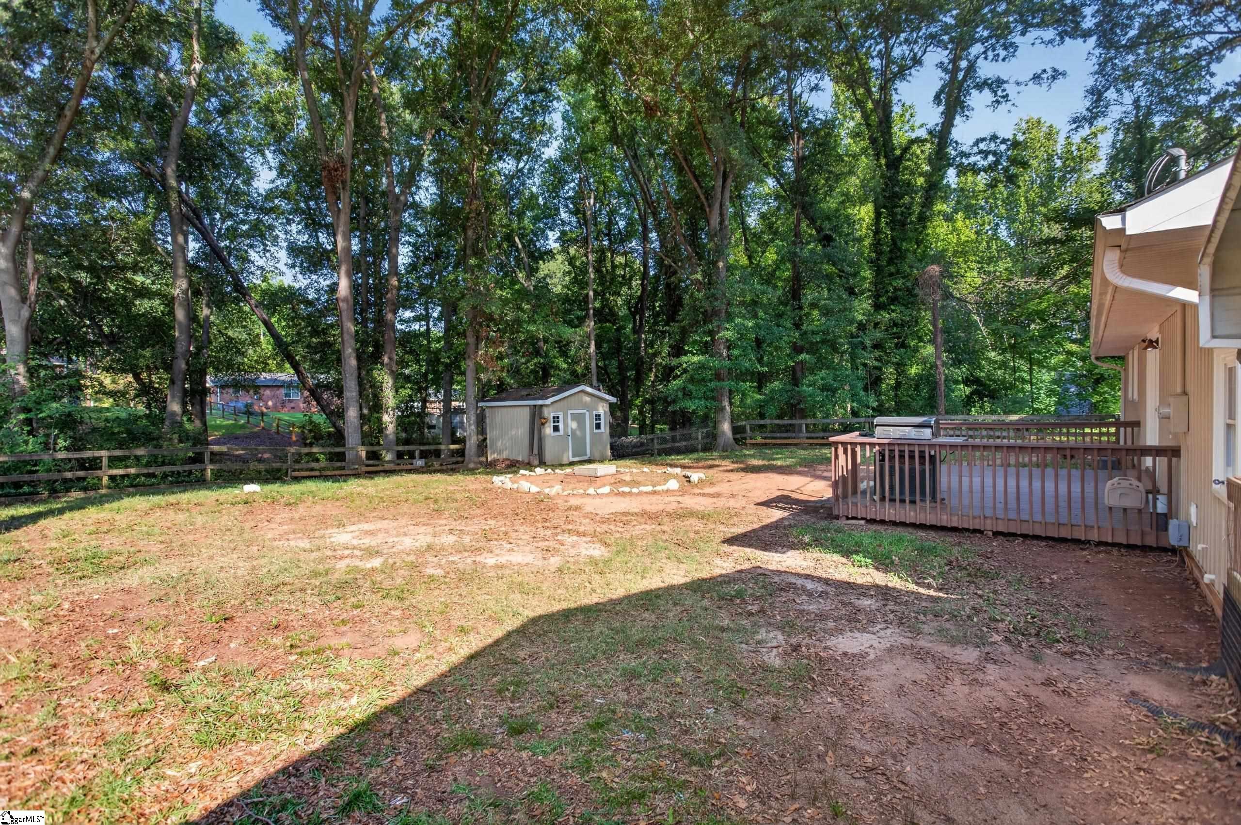 Wooded backyard with a fenced yard, small shed, and deck with a grill