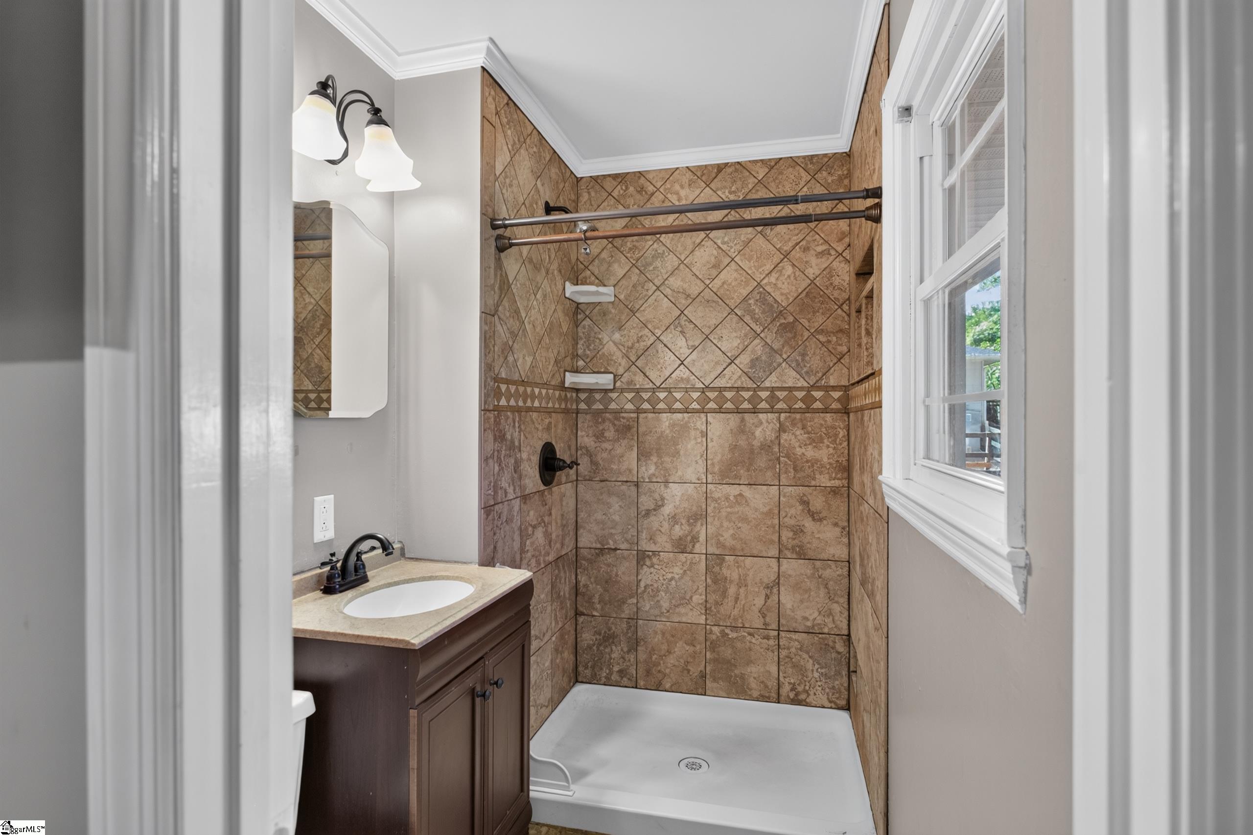 Bathroom with brown tiled walk-in shower, white shower pan, and dark wood vanity beside a window.