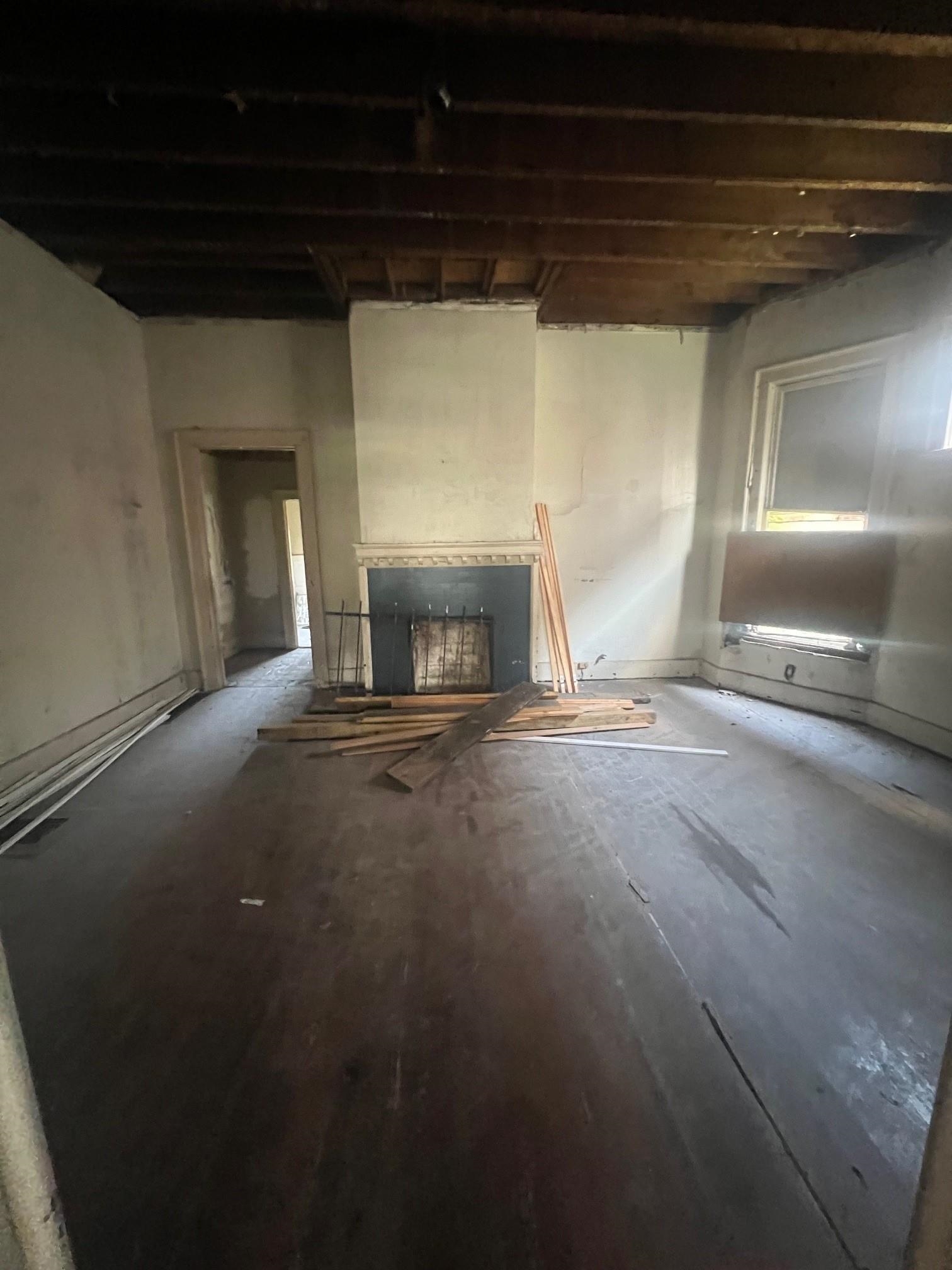 Unfinished living room with a fireplace, exposed ceiling beams, and construction lumber on the floor.