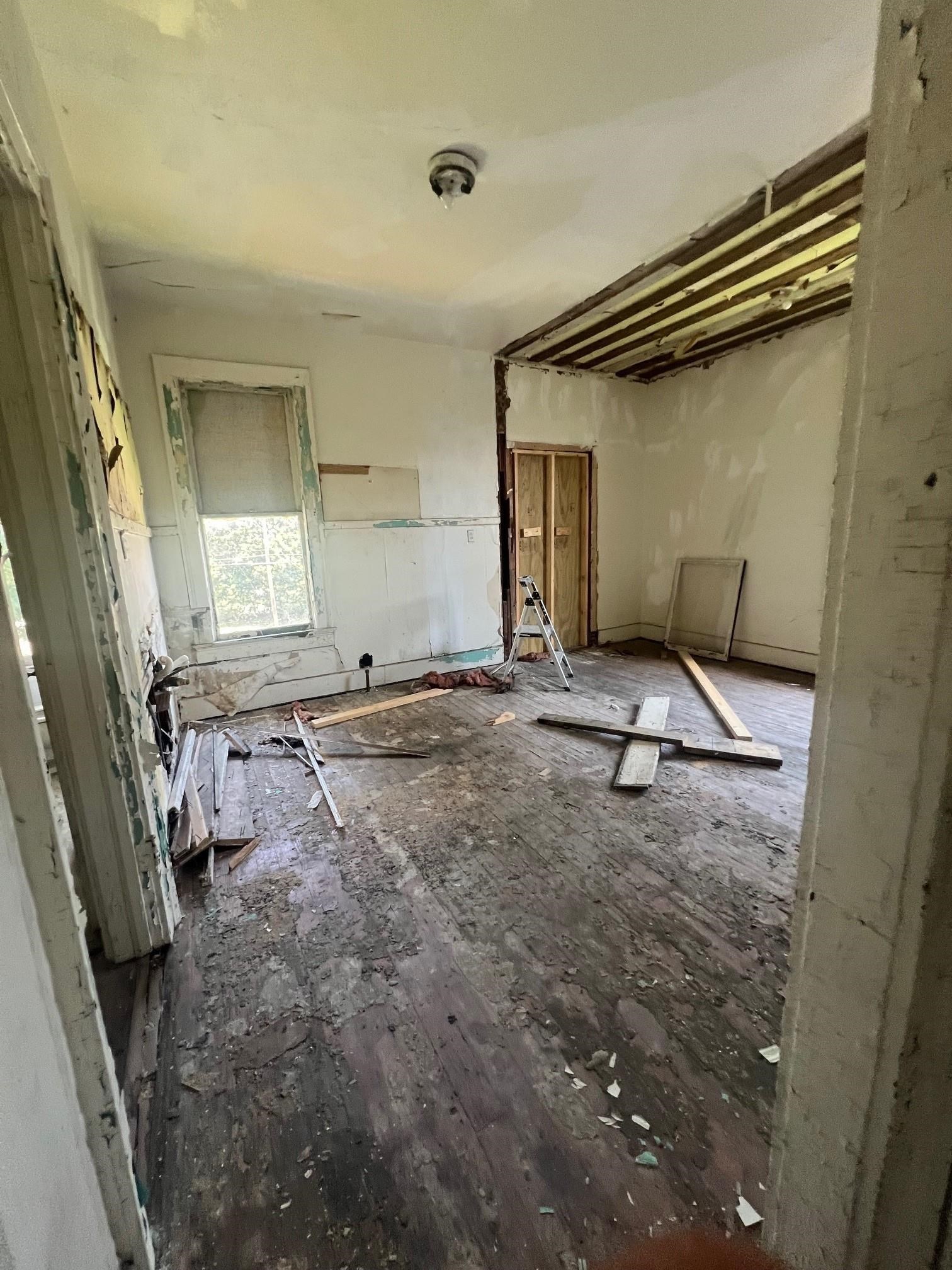 Unfinished room with exposed ceiling joists, stripped walls, and construction debris on a worn wood floor.