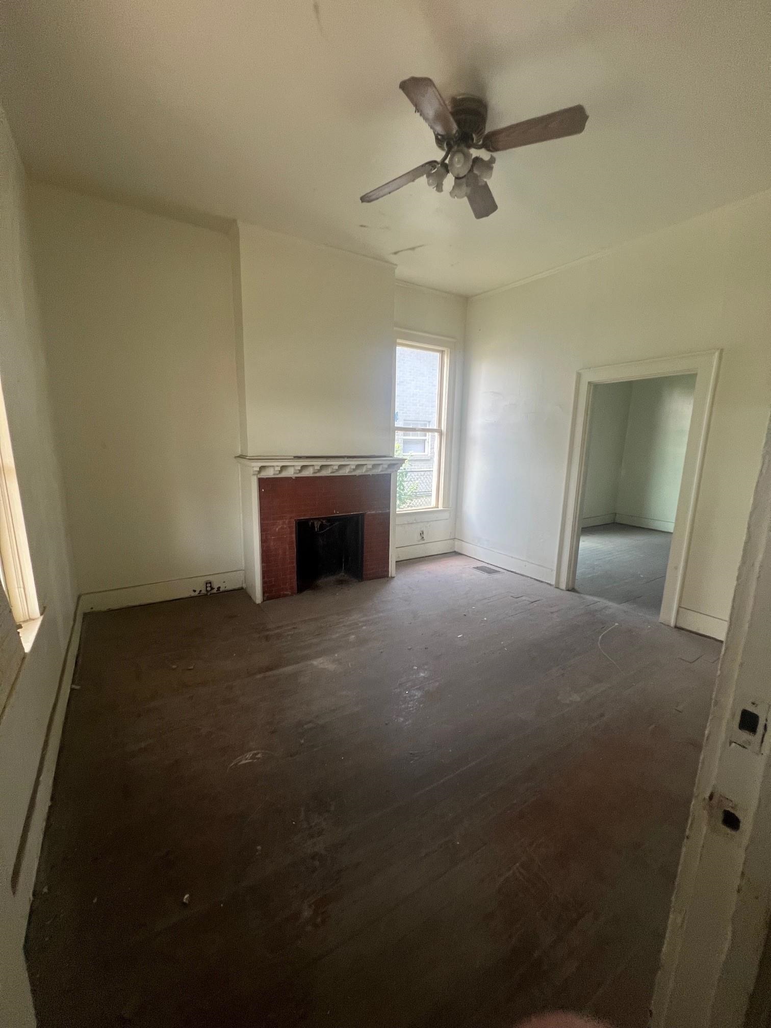 Vacant living room with a brick fireplace, dark hardwood floors, and a ceiling fan.