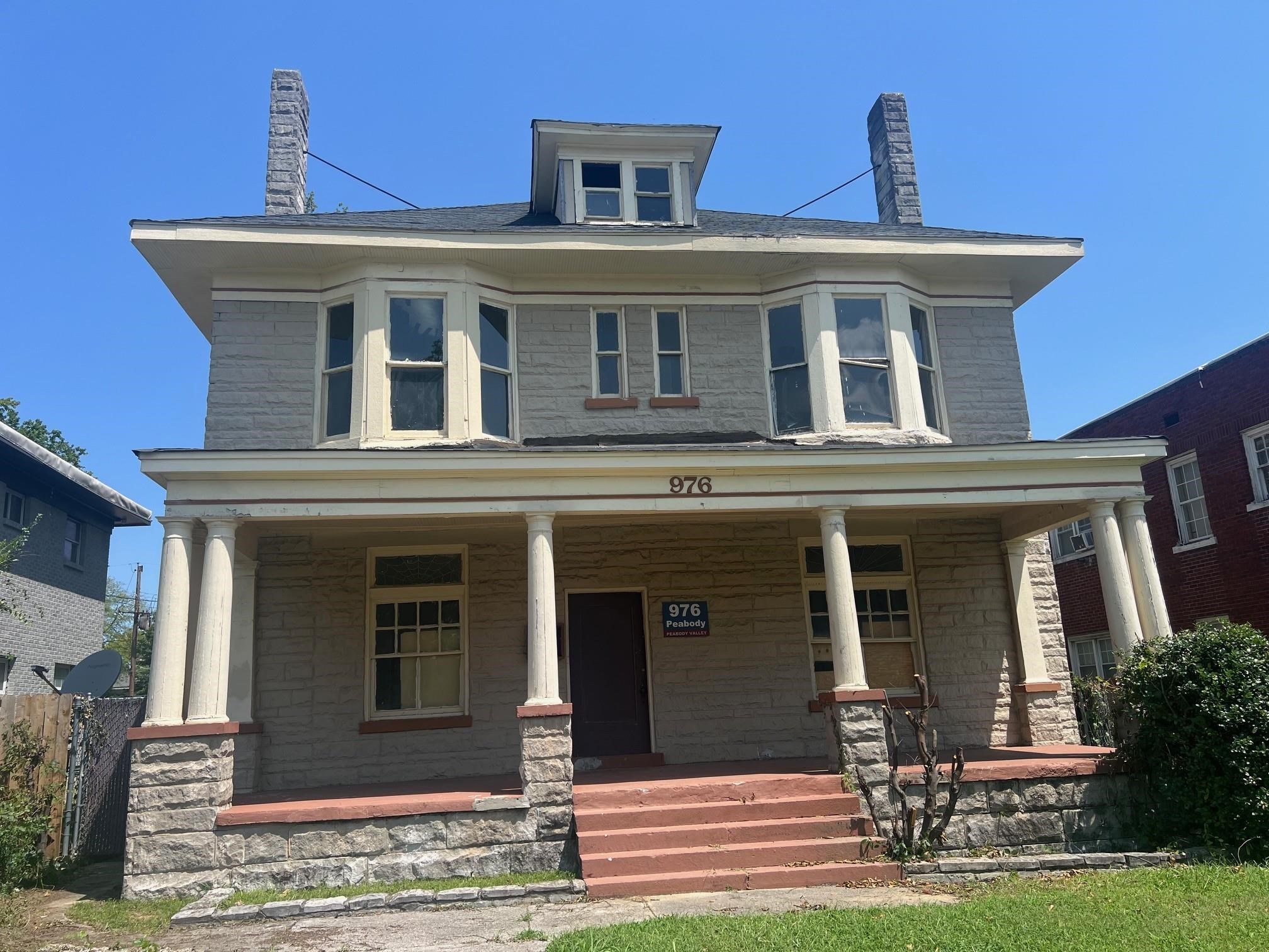 Two-story gray stone house with a columned porch, bay windows, and reddish front steps.