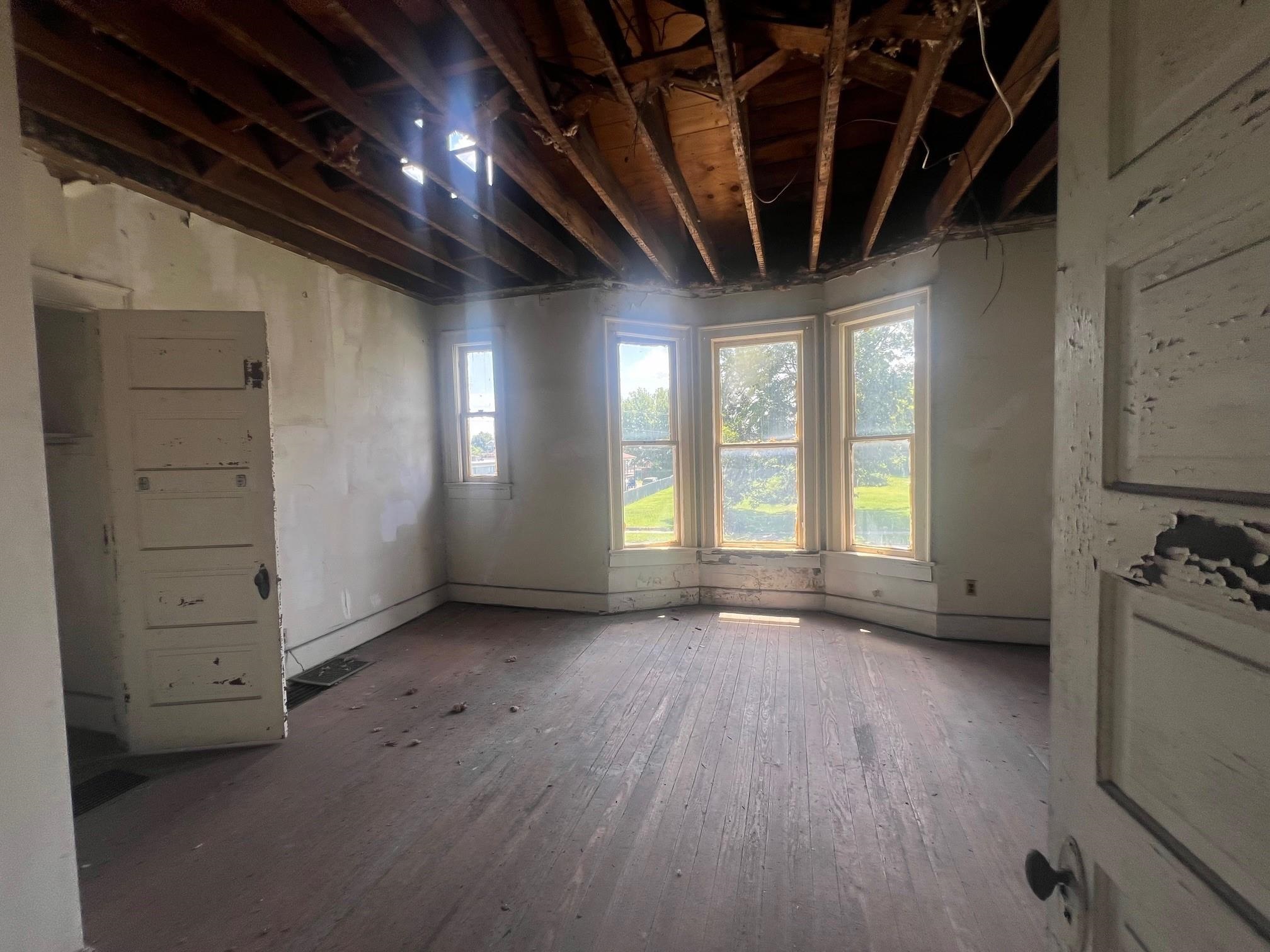 Unfinished room with an exposed wood ceiling, bay windows, and a brick fireplace.