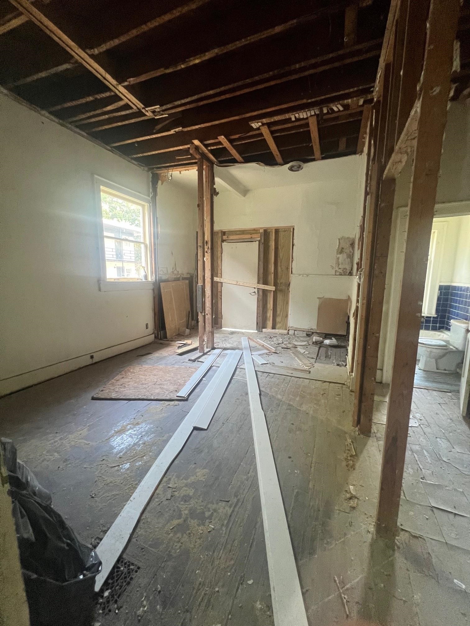Renovated interior with exposed ceiling joists, construction debris, and a bathroom visible through the doorway.