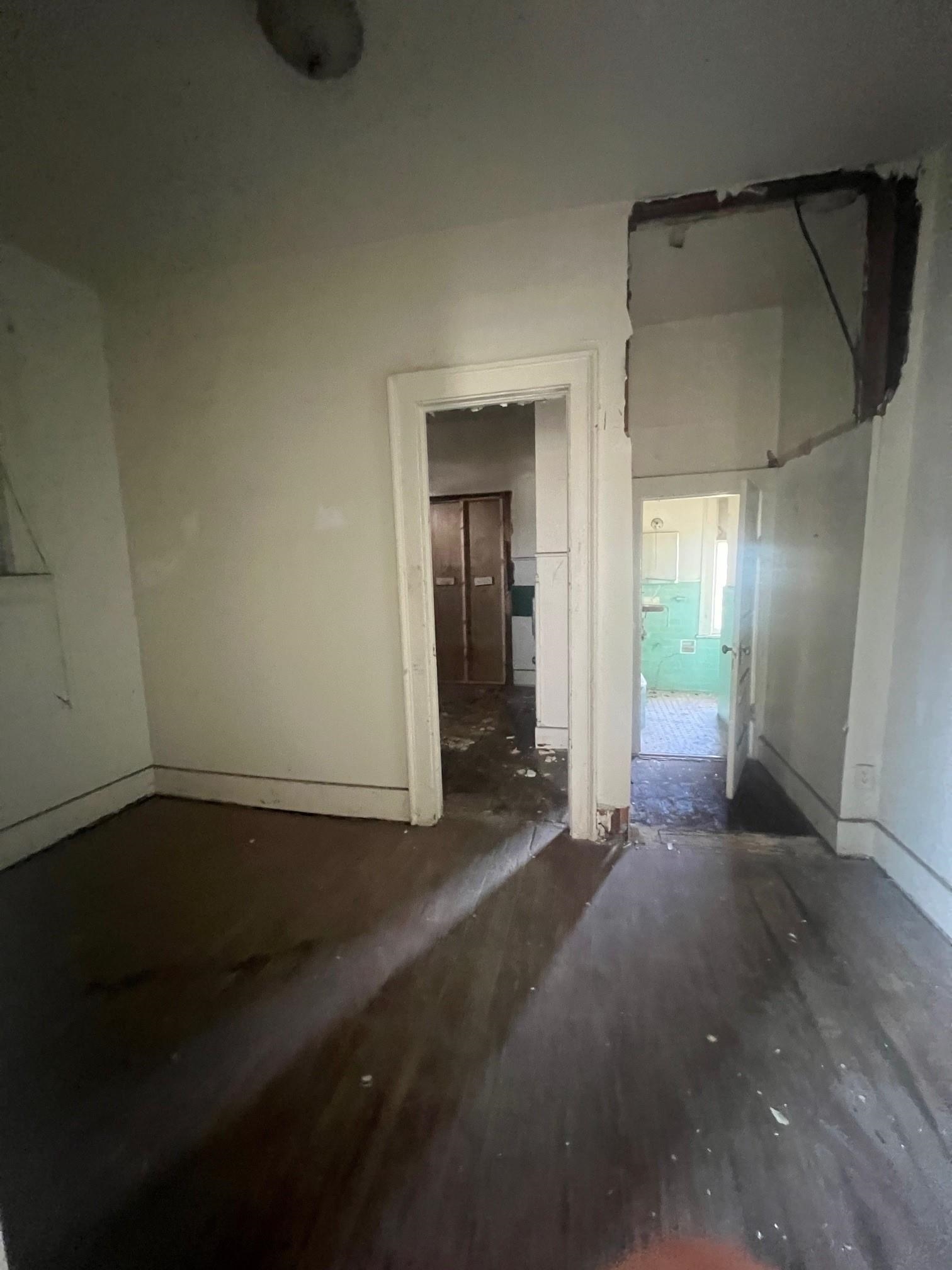 Damaged vacant hallway with dark wood floors and exposed ceiling framing.