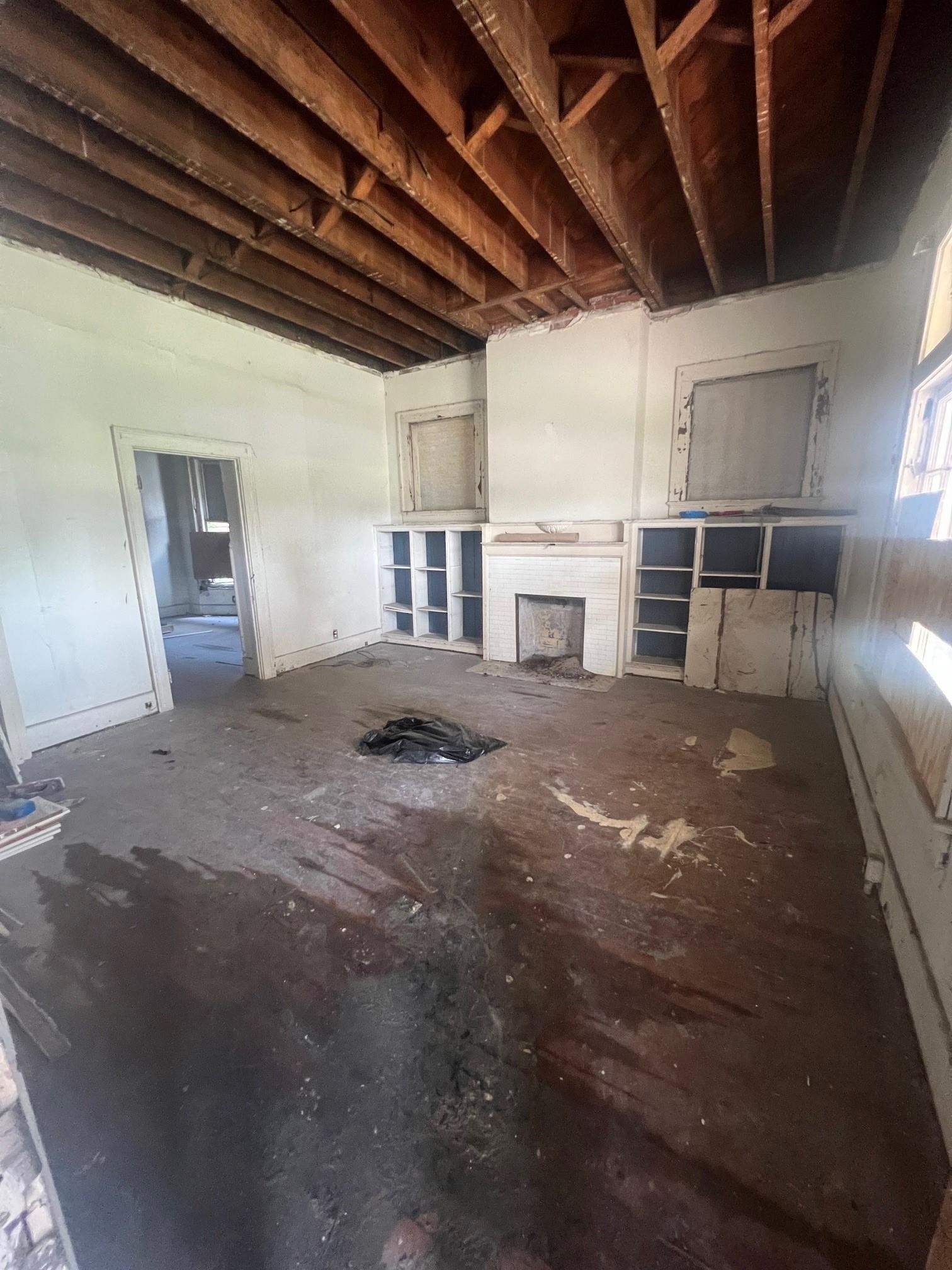 Unfinished room with exposed ceiling joists, a tiled fireplace, and built-in shelving.
