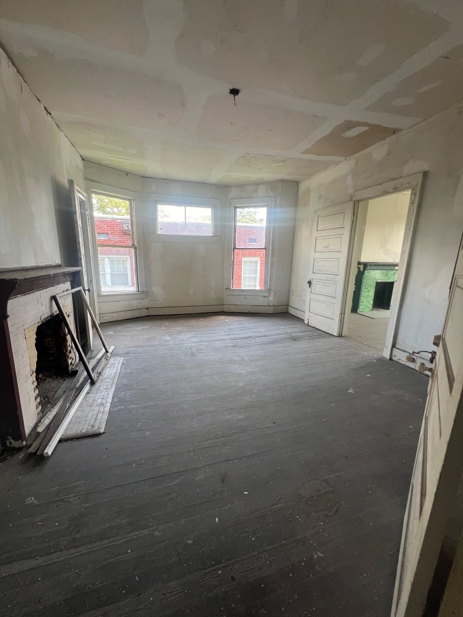 Unfinished room with a white brick fireplace, dark plank floor, and three windows