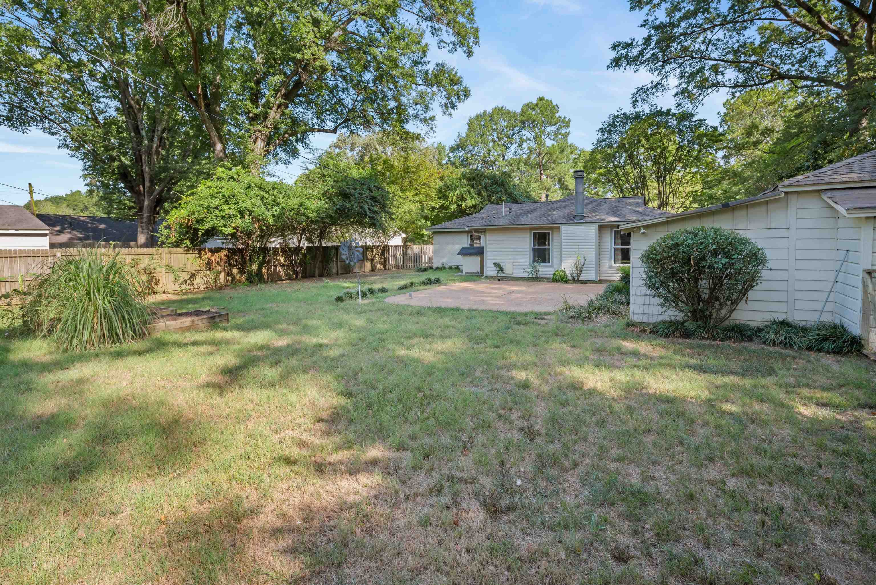 Backyard with a paved patio, grassy yard, mature trees, and wooden fence.