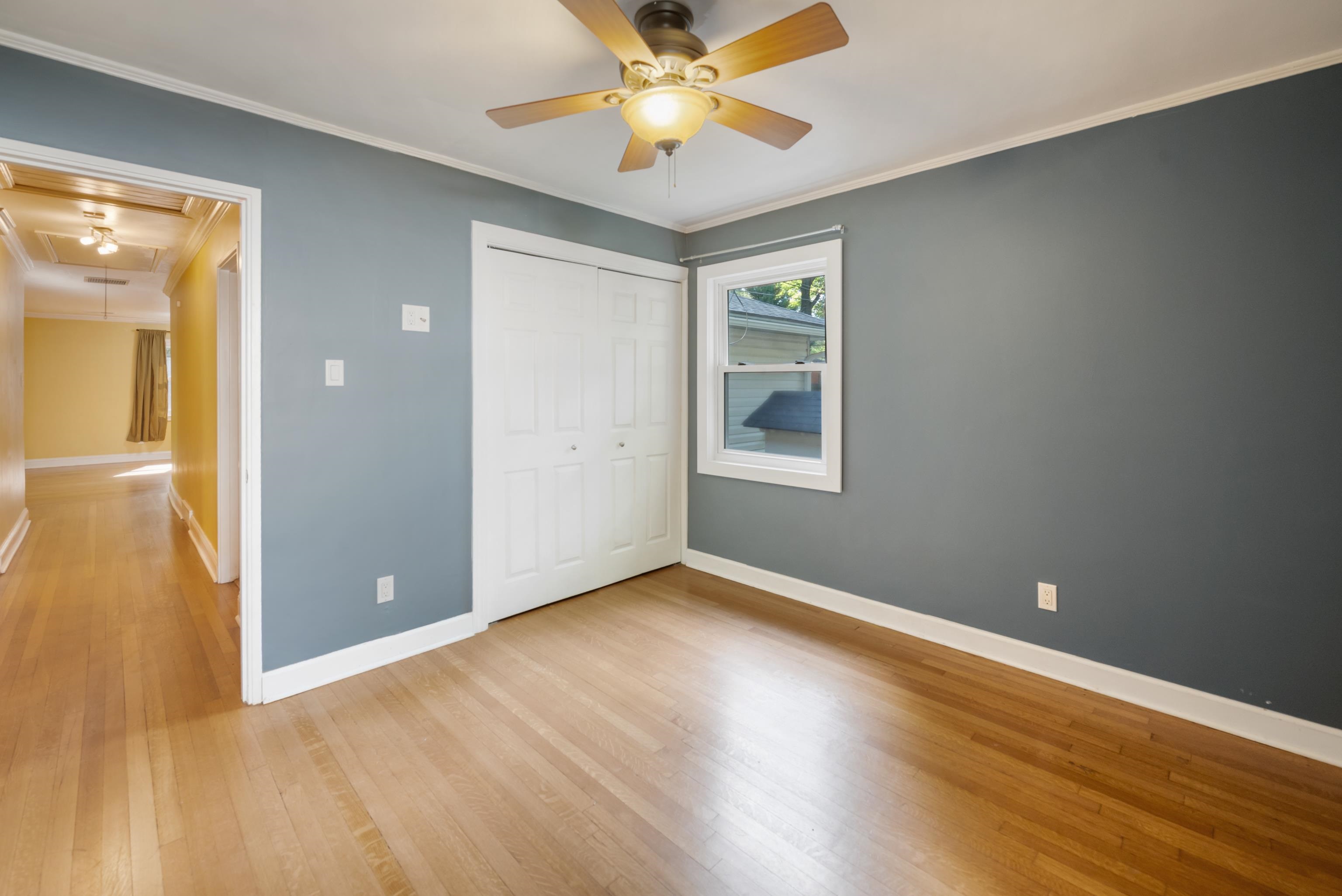 Empty bedroom with gray walls, white closet doors, a ceiling fan, and hardwood floors.