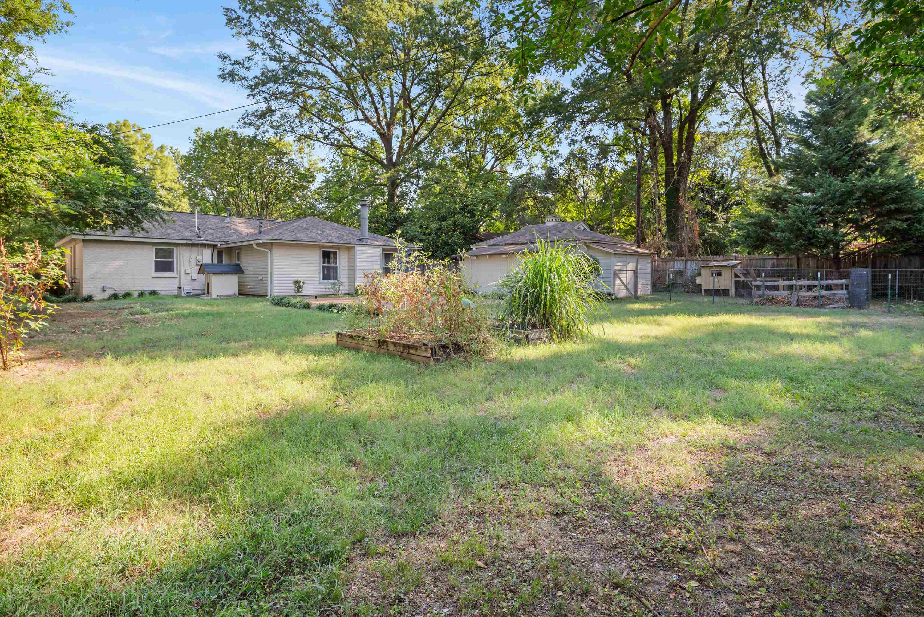 Single-story home behind a grassy backyard with mature trees and a detached outbuilding.