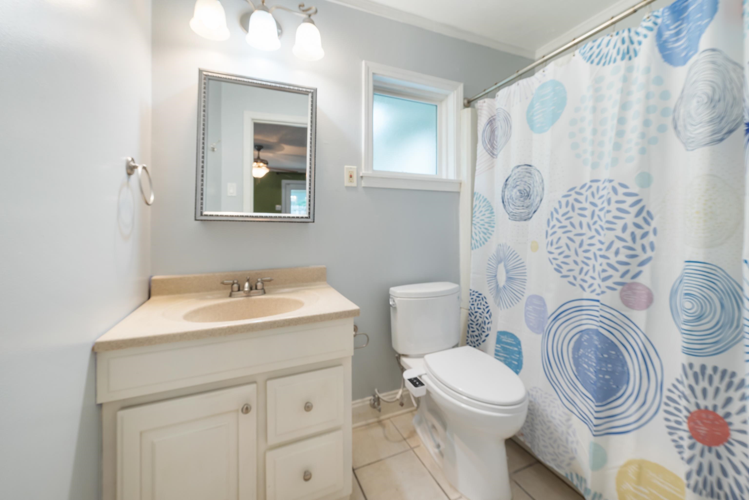 Bathroom with a cream vanity, white toilet, frosted window, and blue patterned shower curtain.