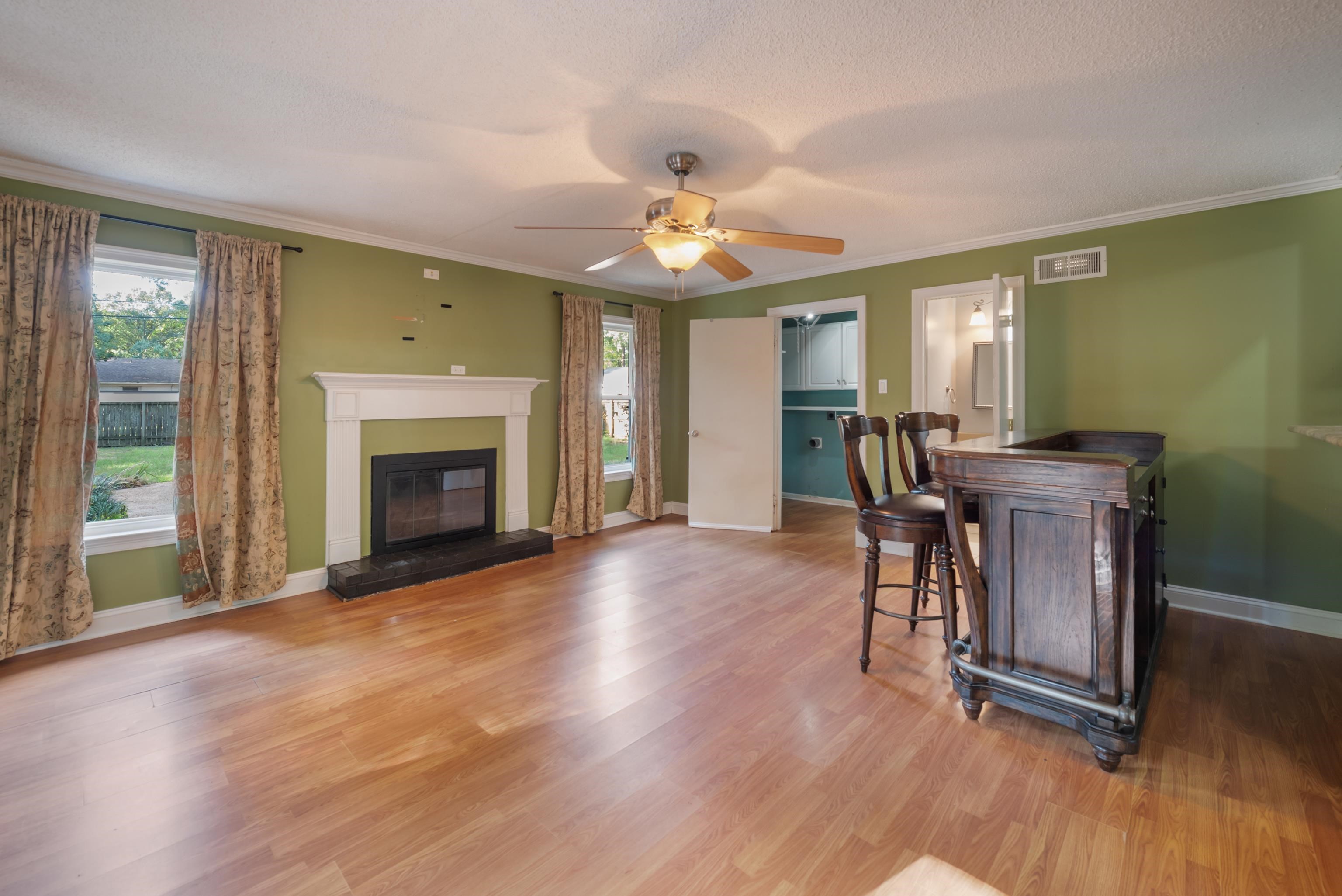 Room with a white fireplace, green walls, wood floors, and a wooden bar with two stools.