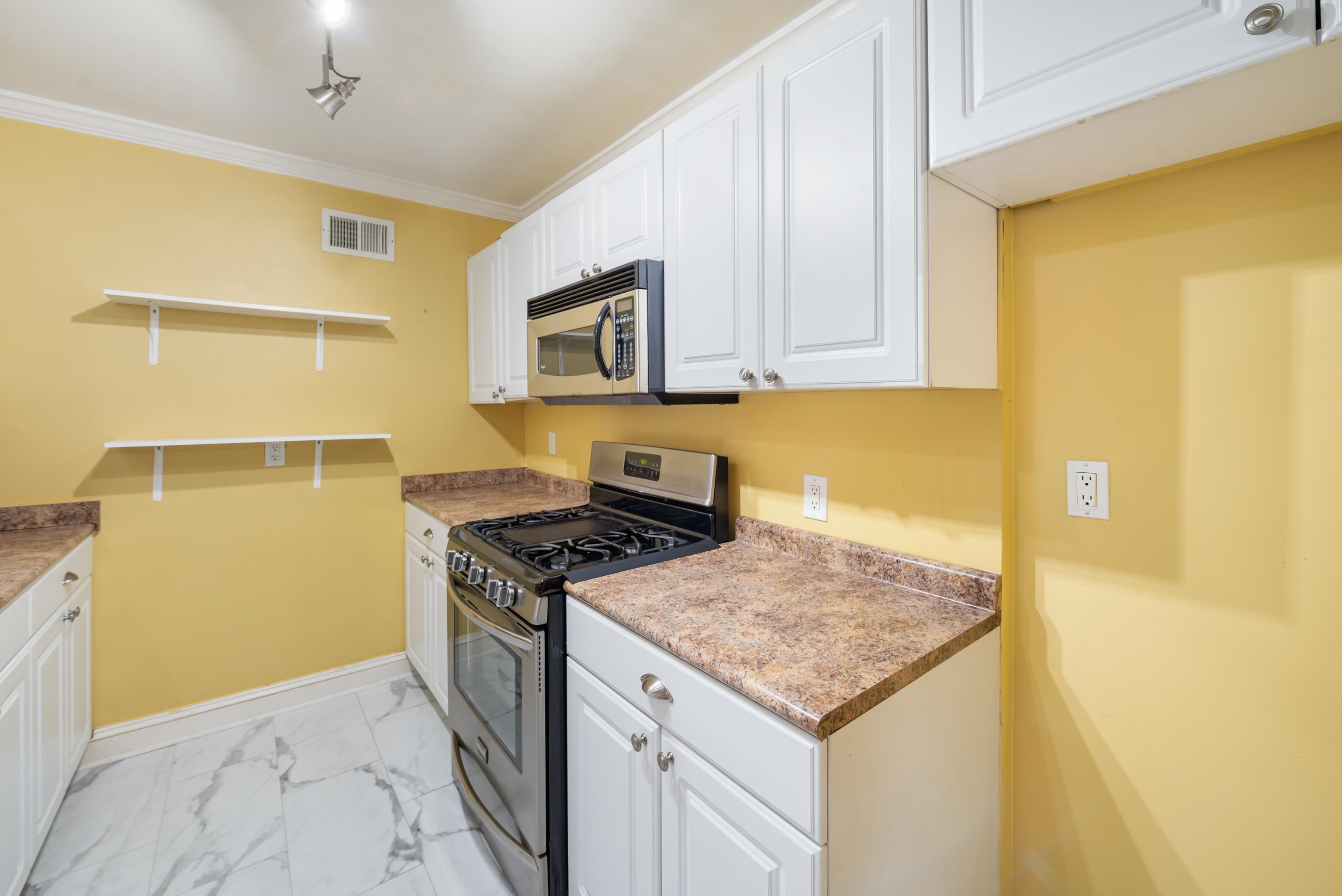 Kitchen with yellow walls, white cabinets, brown countertops, and a stainless steel gas range and microwave.