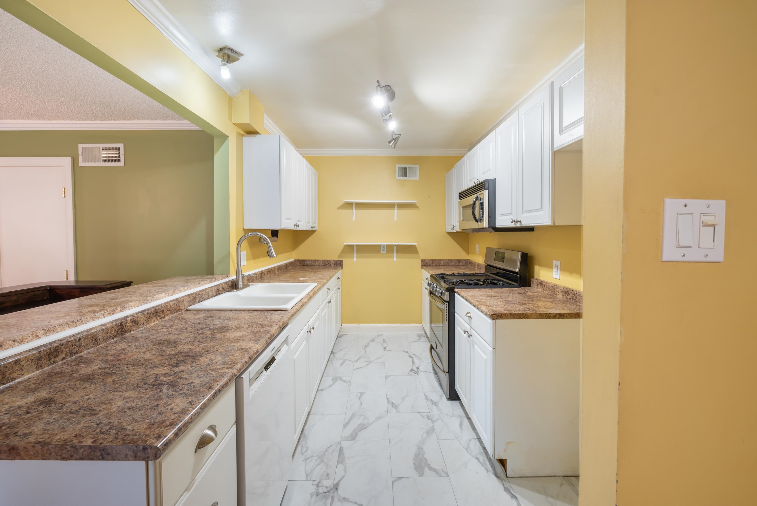 Galley kitchen with white cabinets, brown countertops, and large marble-look floor tiles.