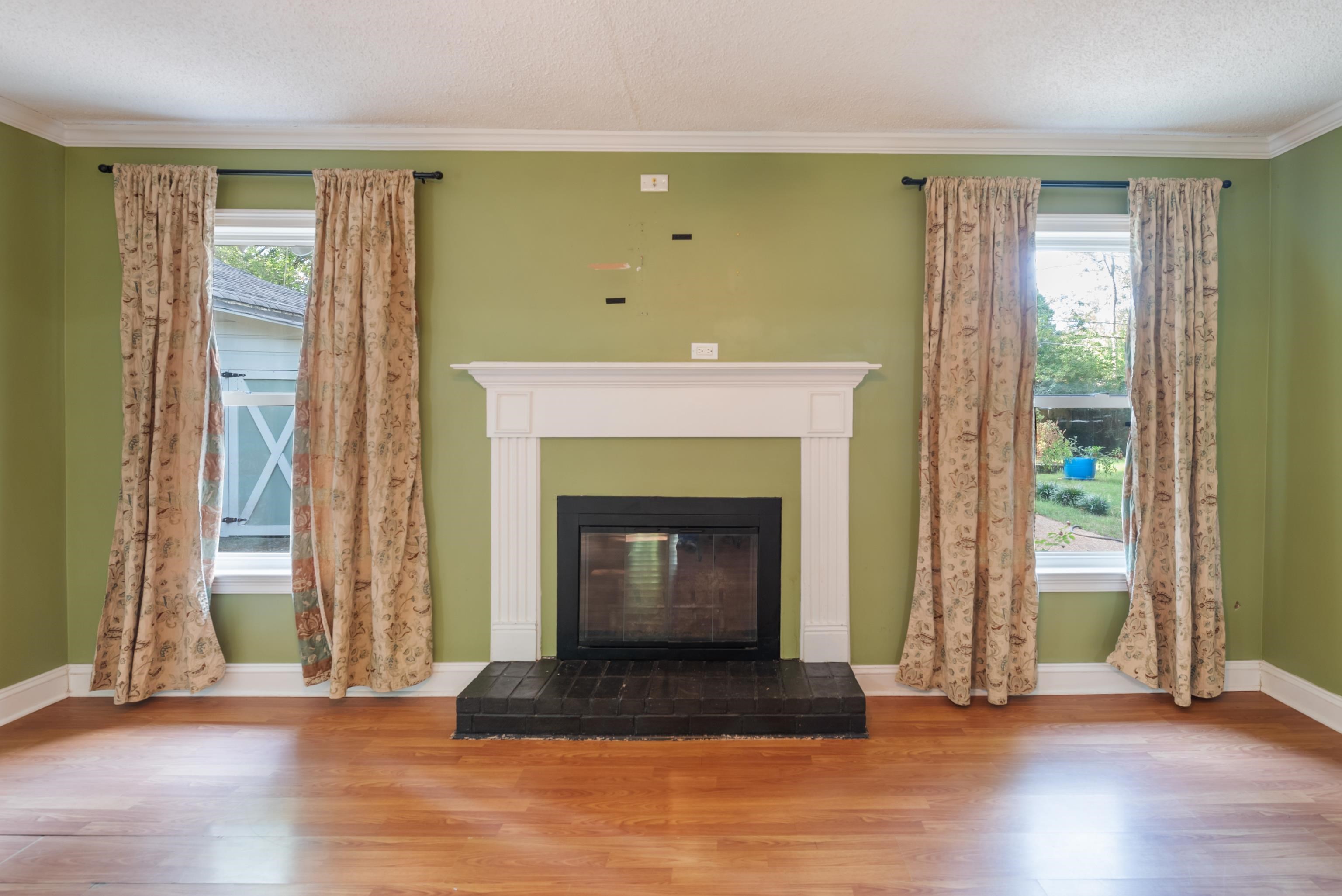 Living room with a white fireplace, hardwood floors, and curtained windows.
