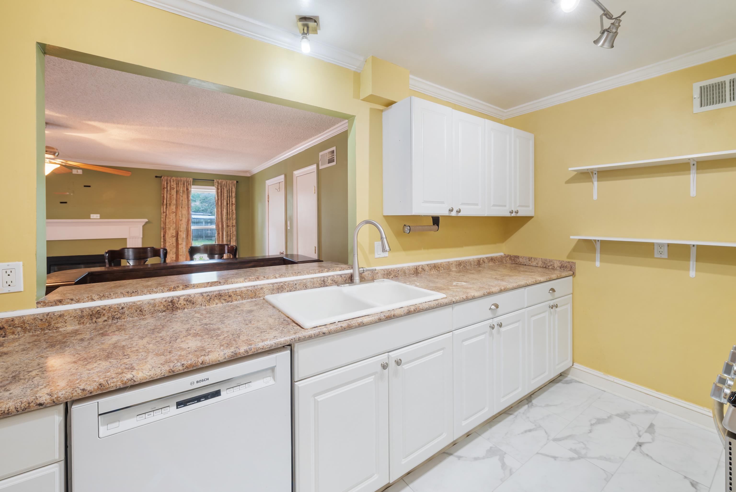 Kitchen with white cabinets, a long mottled countertop, and a sink beneath open wall shelves.