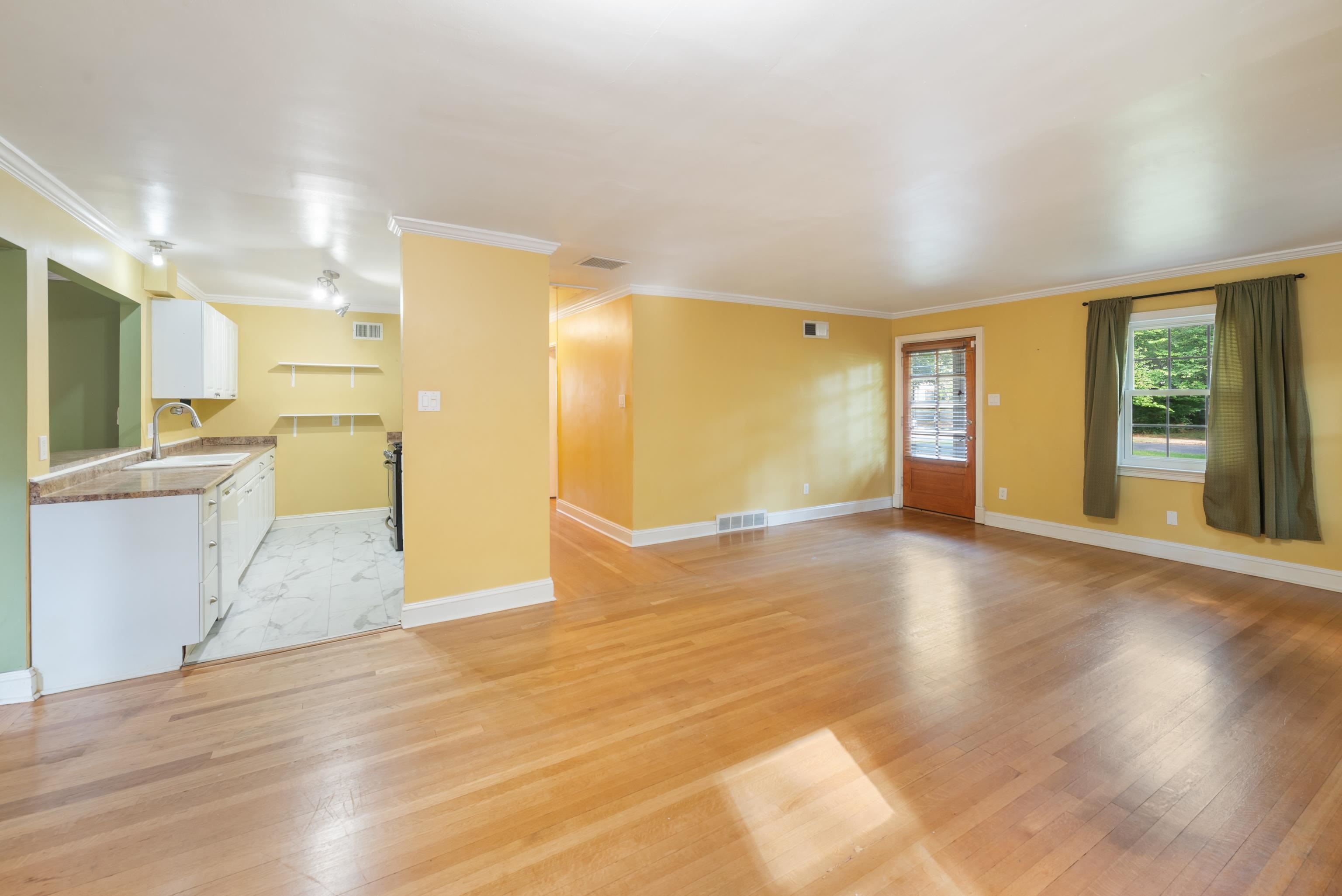 Open living and dining area with yellow walls, hardwood floors, and an adjoining compact kitchen.