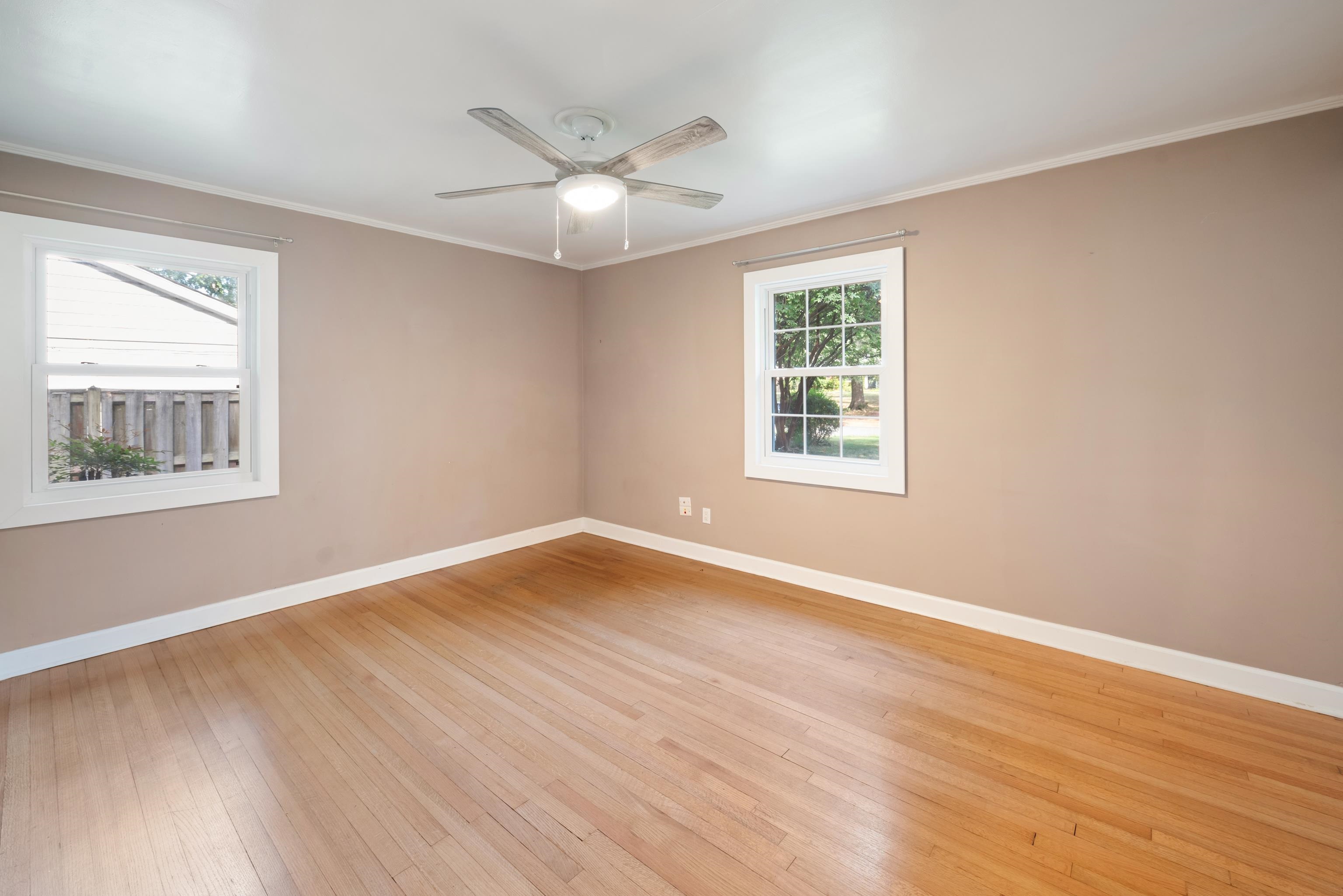 Empty bedroom with hardwood floors, two windows, and a ceiling fan.