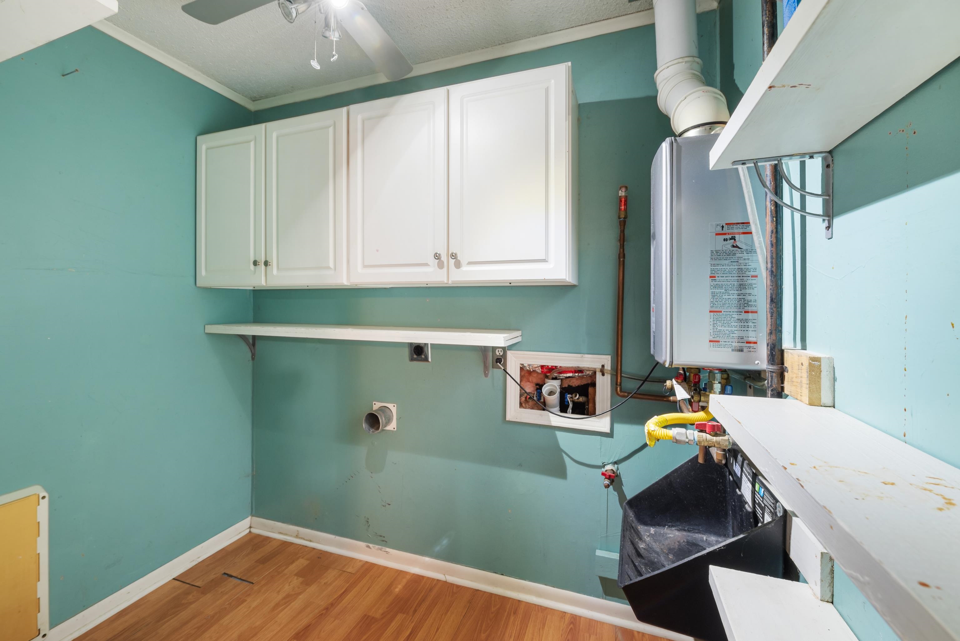 Utility room with teal walls, white cabinets, and an exposed water heater.