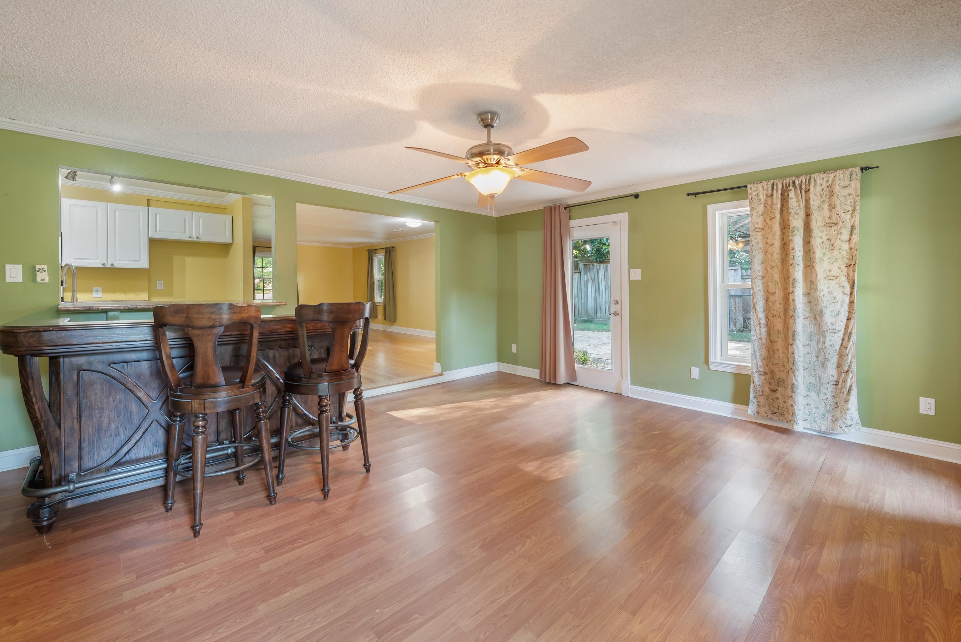 Dining area with a dark wood bar and stools, green walls, and light wood flooring.