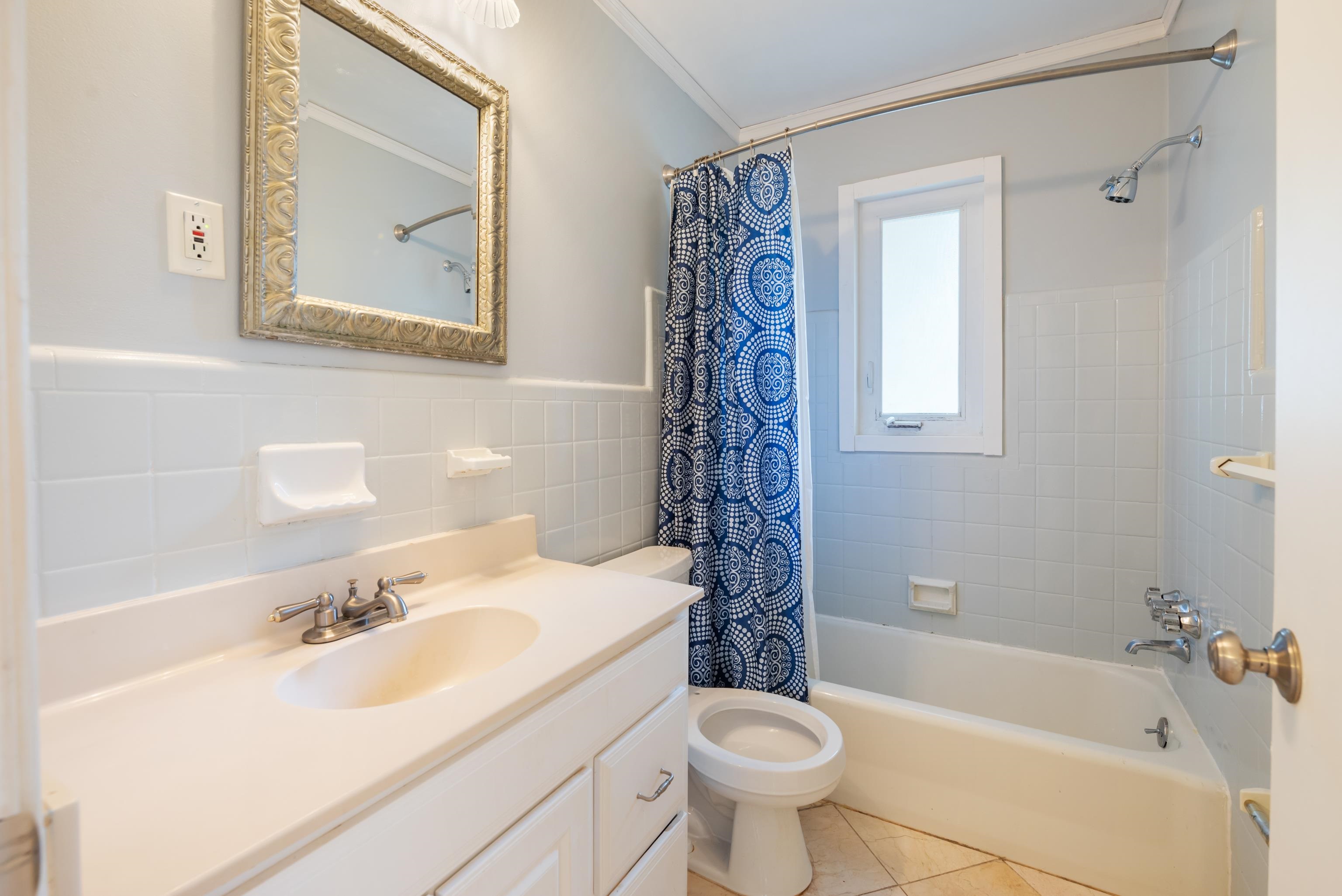 Bathroom with a white vanity, toilet, and tub behind a blue patterned shower curtain.