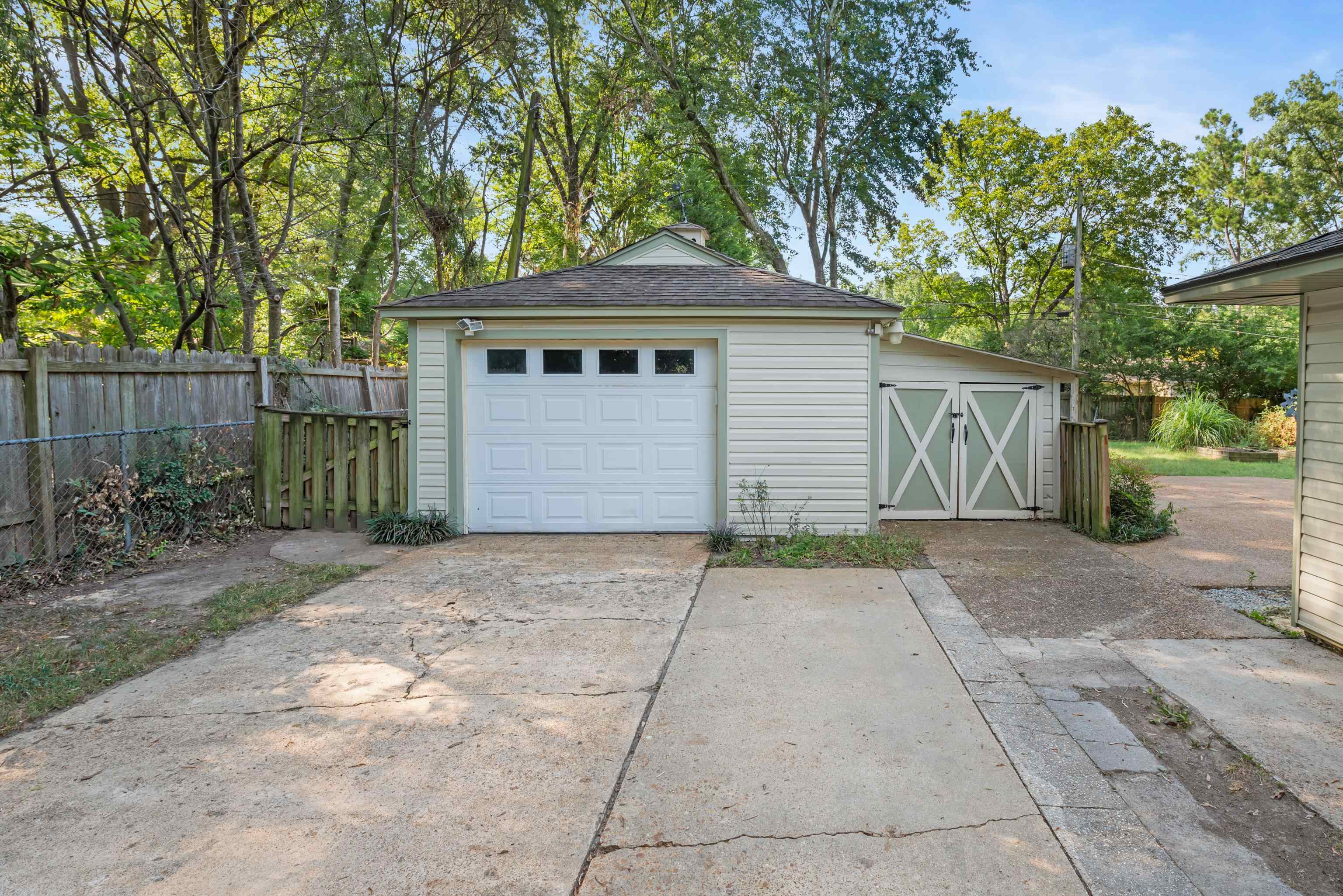 Detached garage with a white overhead door and adjoining double barn doors, at the end of a concrete driveway.