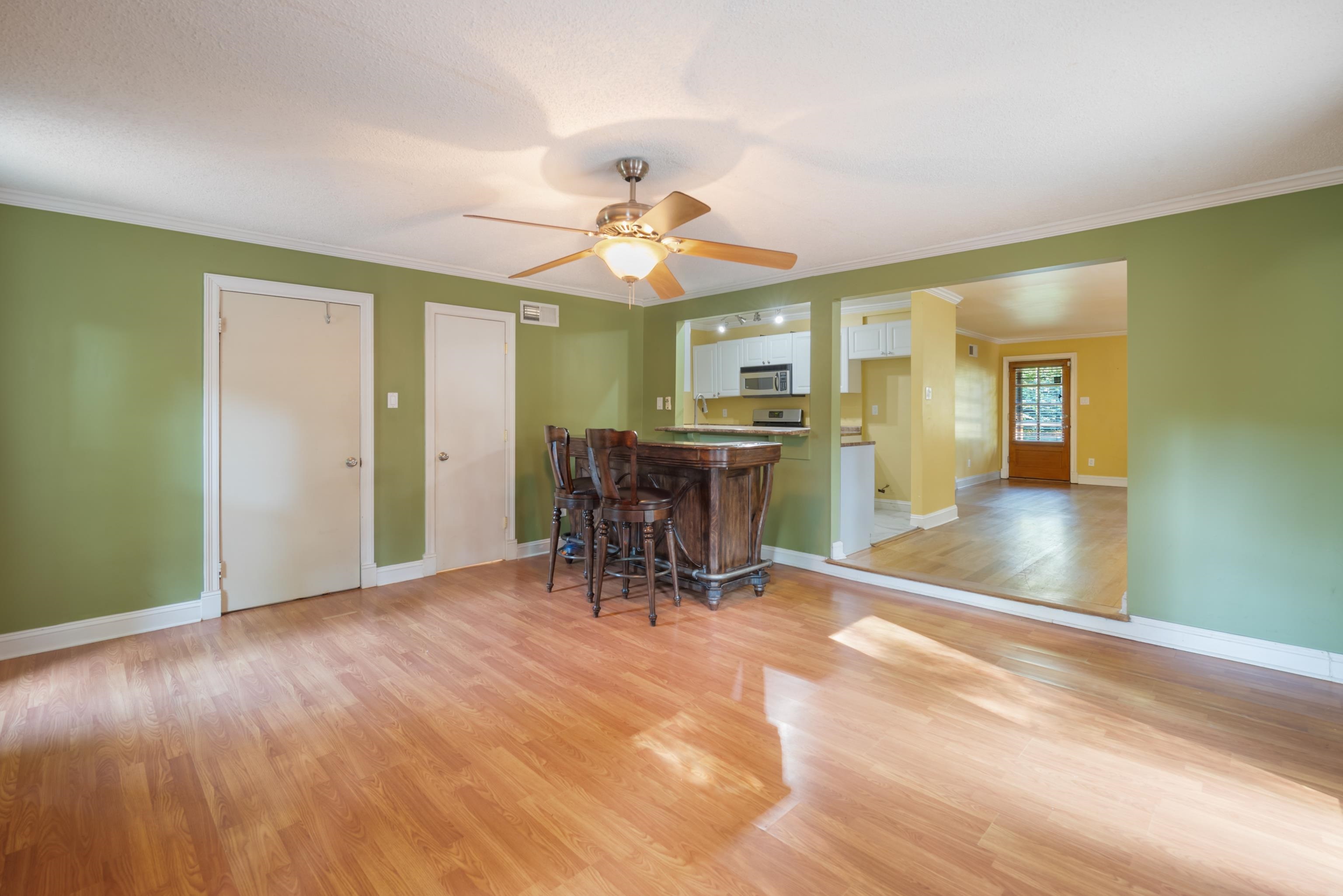 Dining area with green walls, hardwood floors, and a dark wood table and stools beside the kitchen.