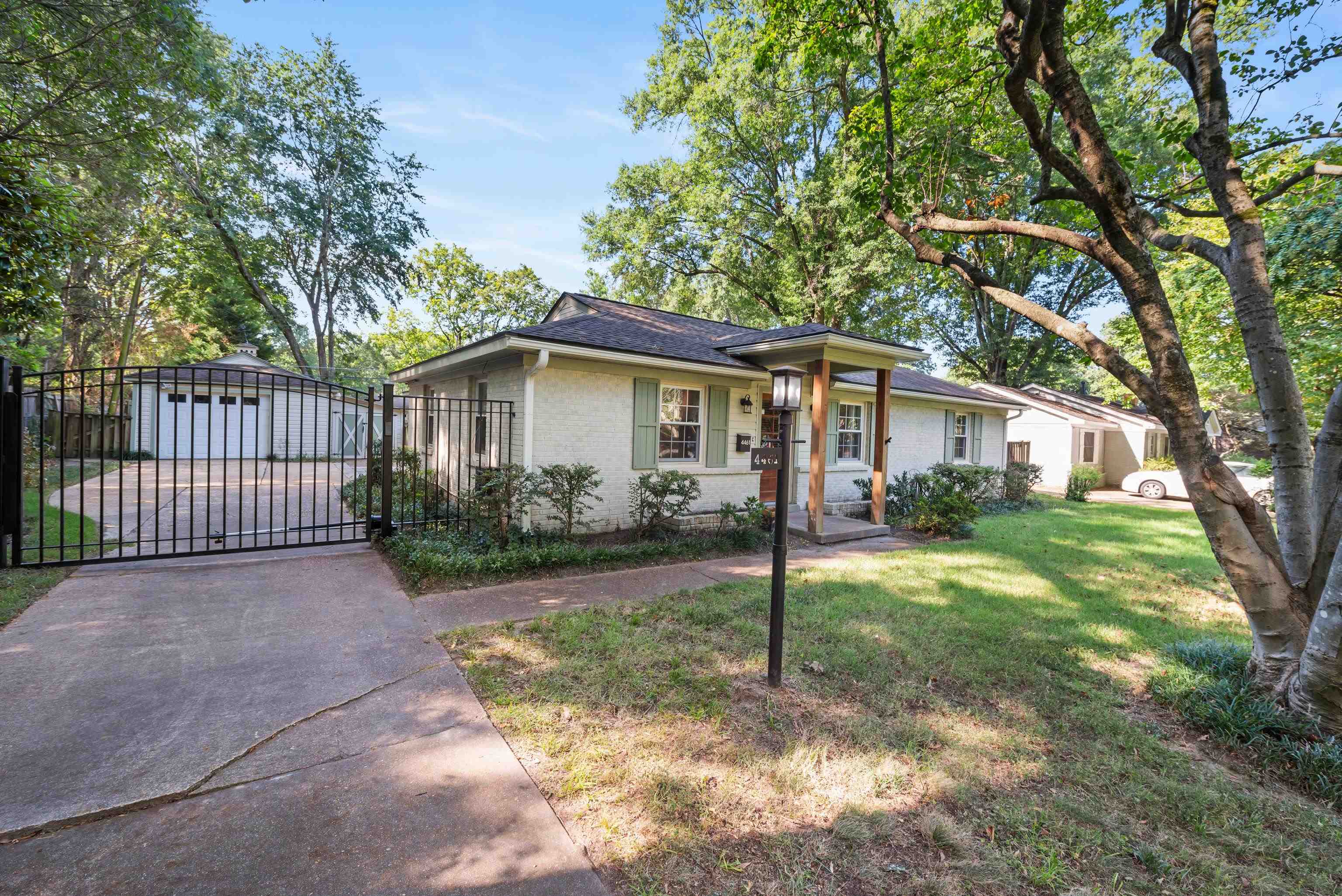 White-brick ranch home with a covered entry, mature trees, and a gated driveway.