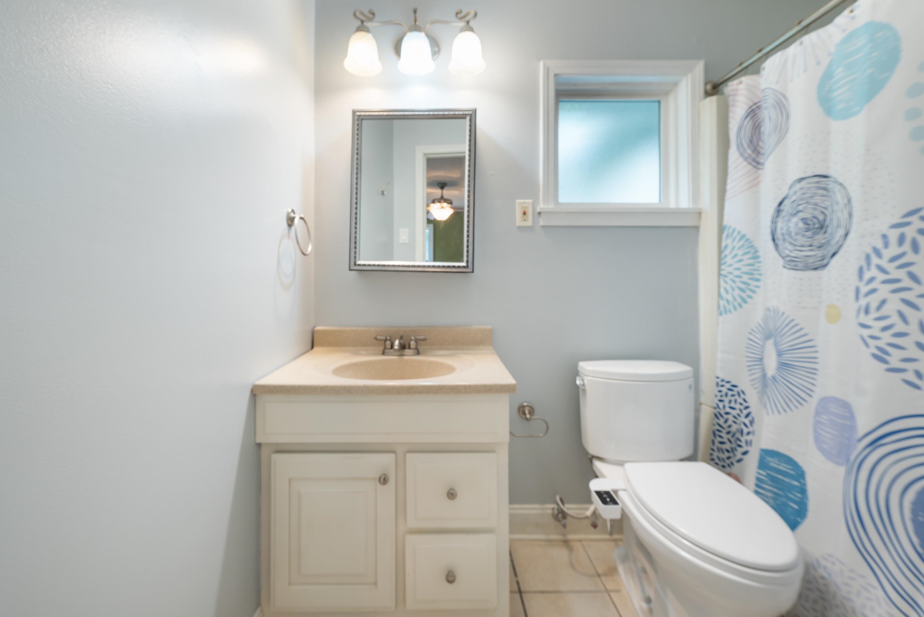 Bathroom with cream vanity and toilet beside a blue patterned shower curtain.