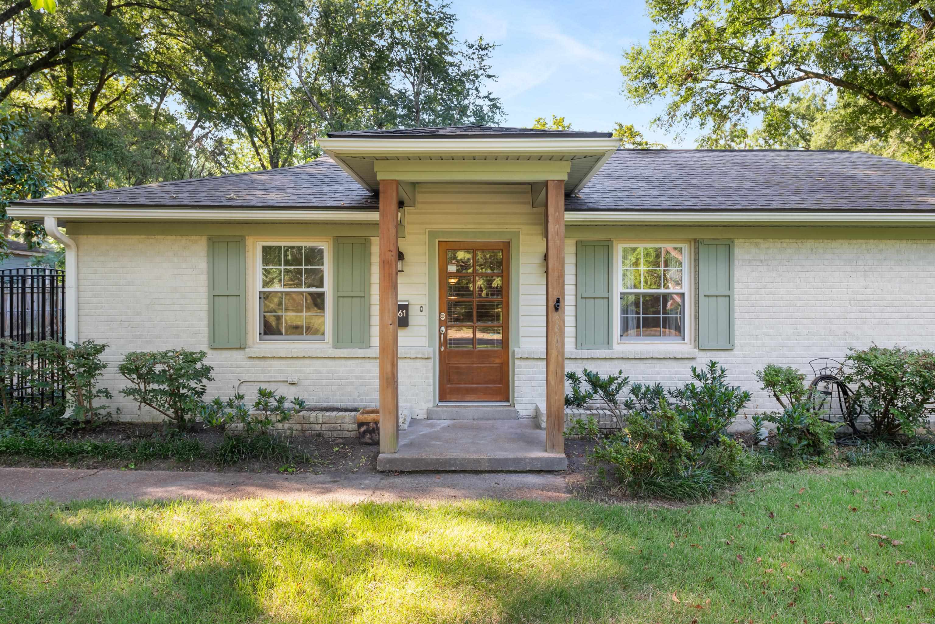 Single-story white brick home with pale green shutters and a covered wood-post entry porch.