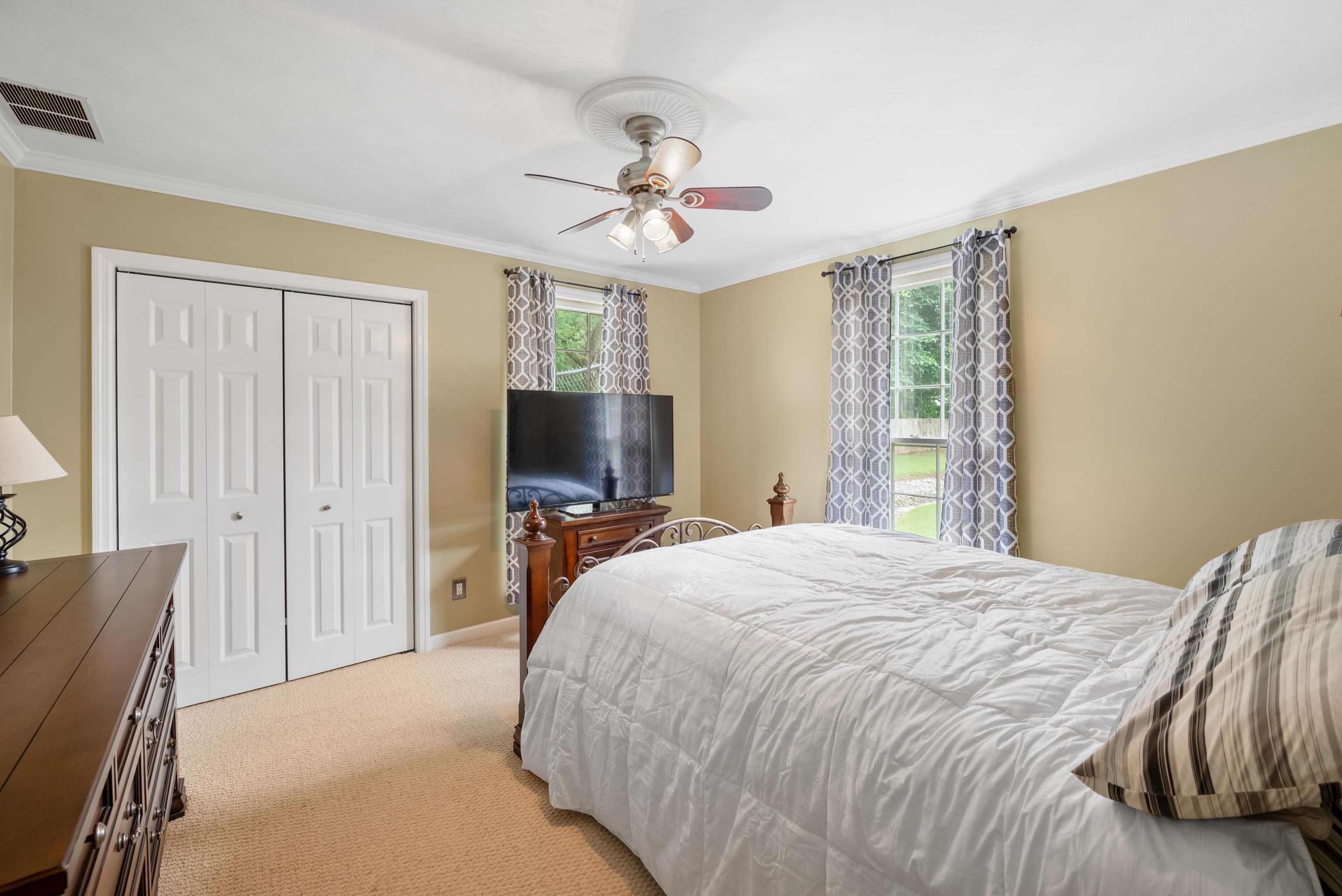 Furnished bedroom with a large white bed, patterned curtains, and a ceiling fan.