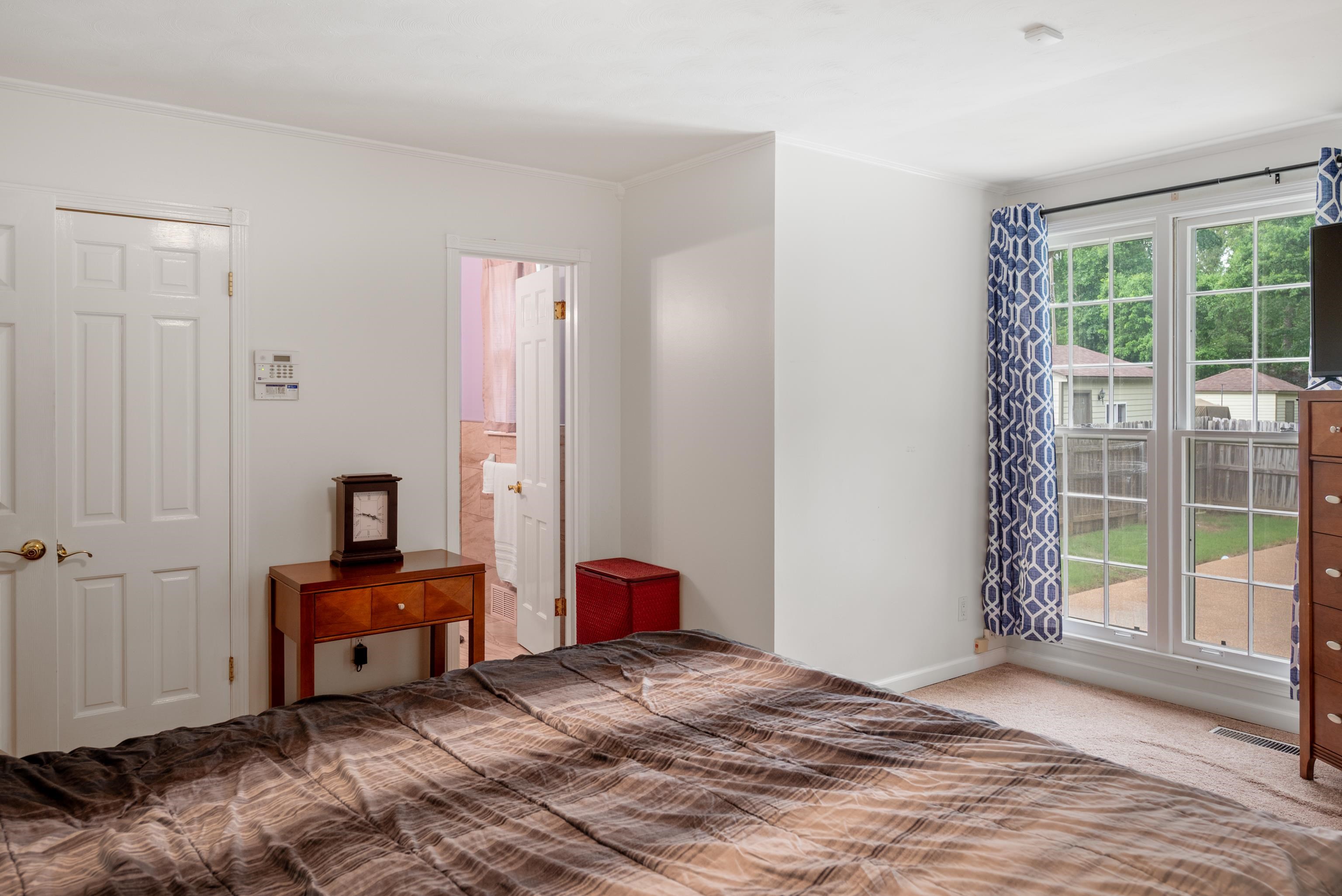 Bedroom with a large brown-patterned bedspread and tall windows overlooking a fenced backyard.