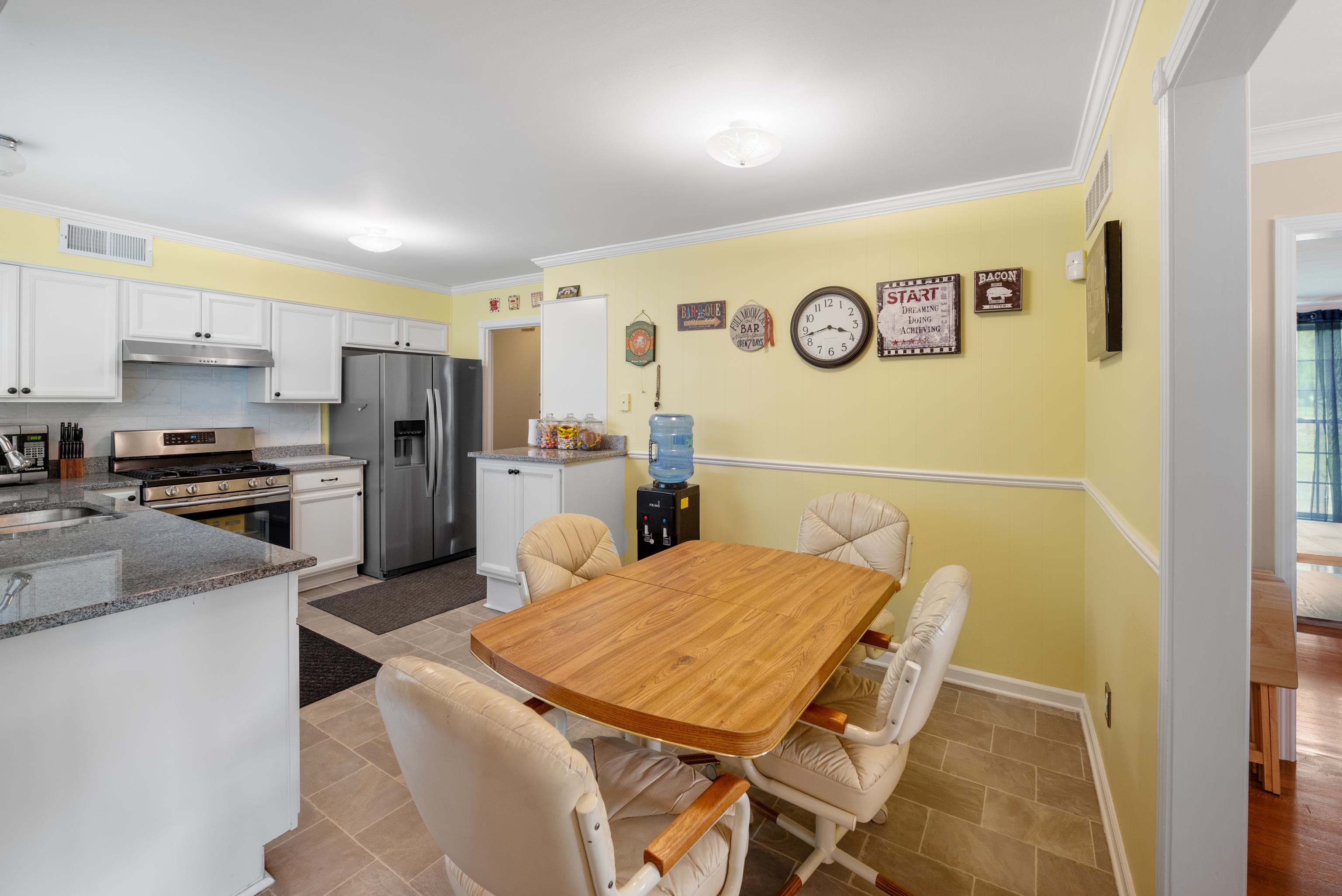 Kitchen and dining area with stainless steel appliances, yellow walls, and a wooden table with cushioned chairs.